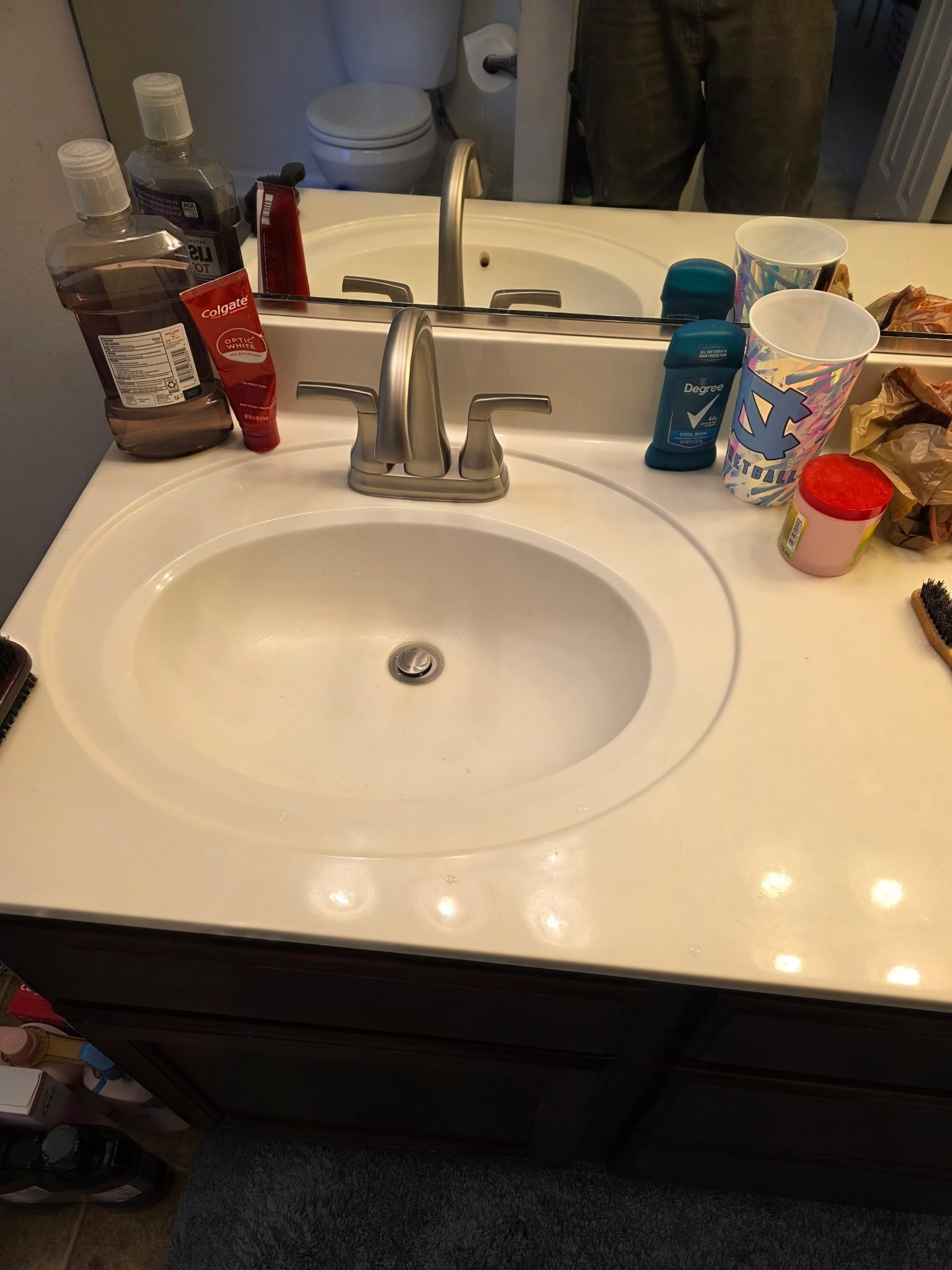 White oval drop-in bathroom sink with a brushed nickel faucet and toiletries on the counter.