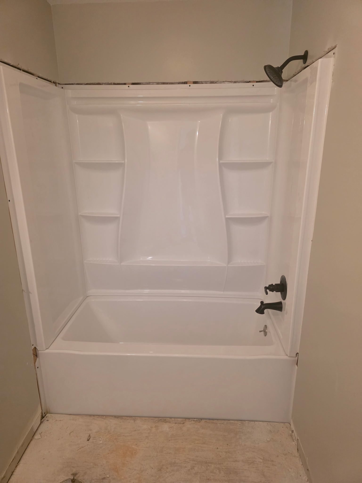 White fiberglass tub-shower combo with an oil-rubbed bronze shower head, faucet, and valve in a finished bathroom.