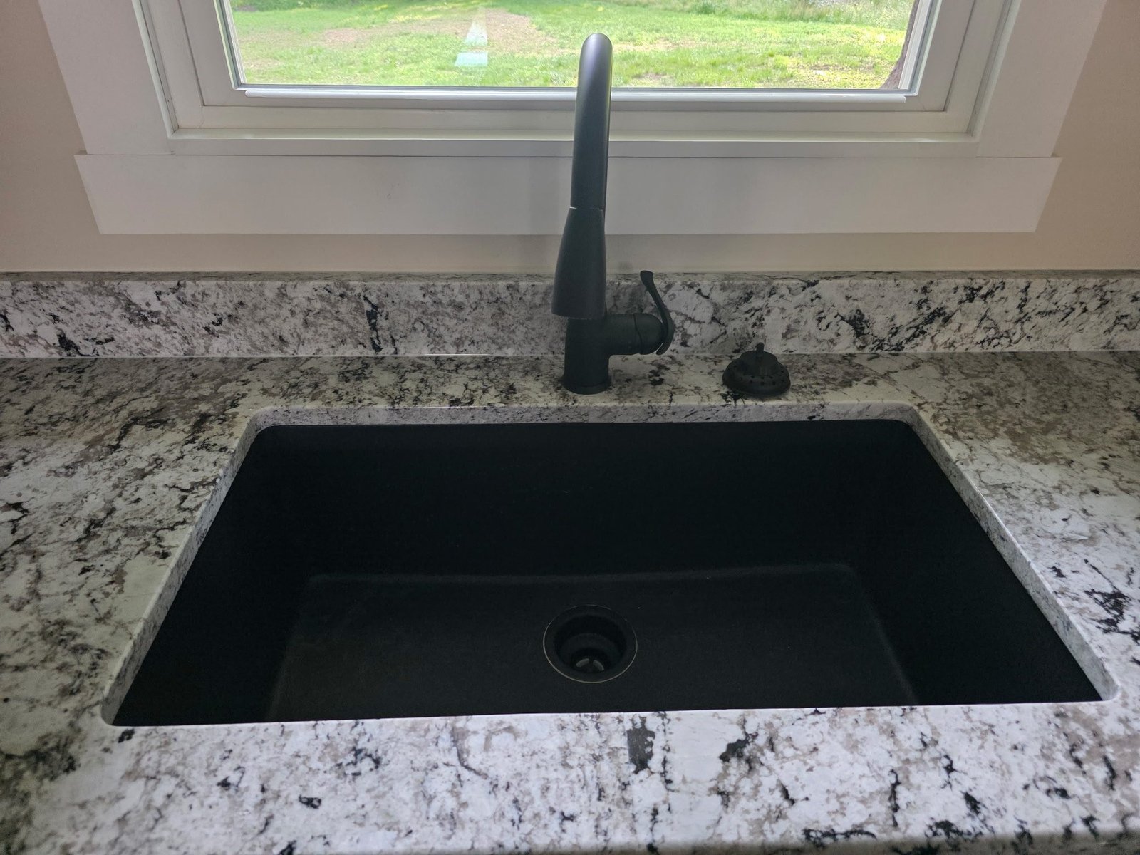 Black granite composite undermount kitchen sink with a matte black faucet installed below a window.