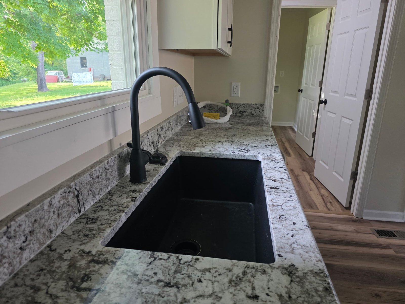 Black granite composite kitchen sink with a matte black gooseneck faucet on a granite countertop.