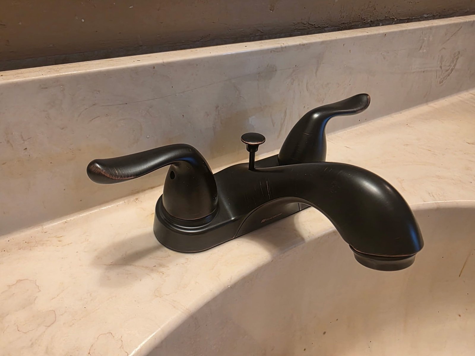Oil-rubbed bronze two-handle bathroom faucet mounted on a marble-look sink basin.