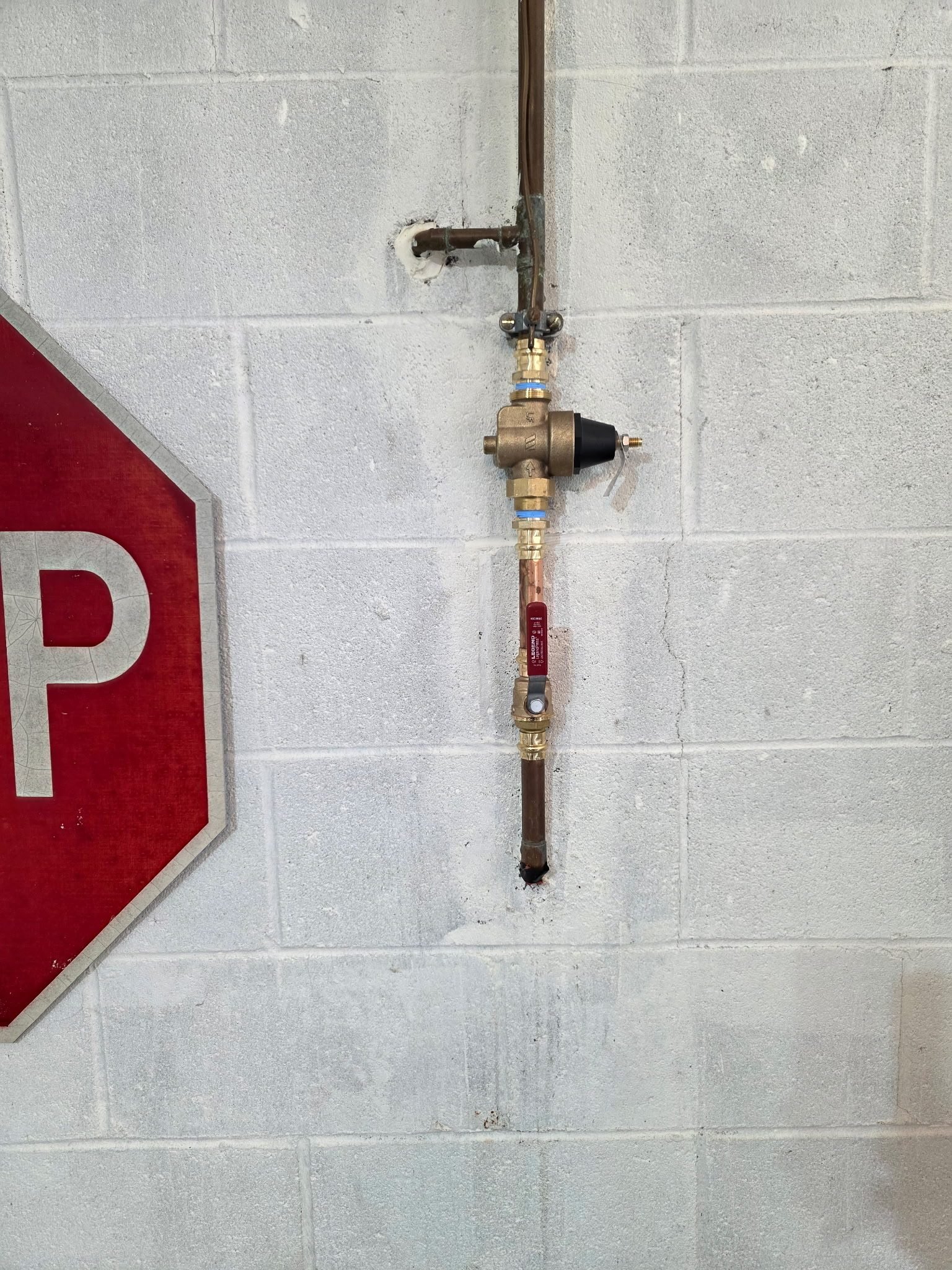 Copper supply line with brass shutoff valves and a pressure-reducing valve mounted on a wall.