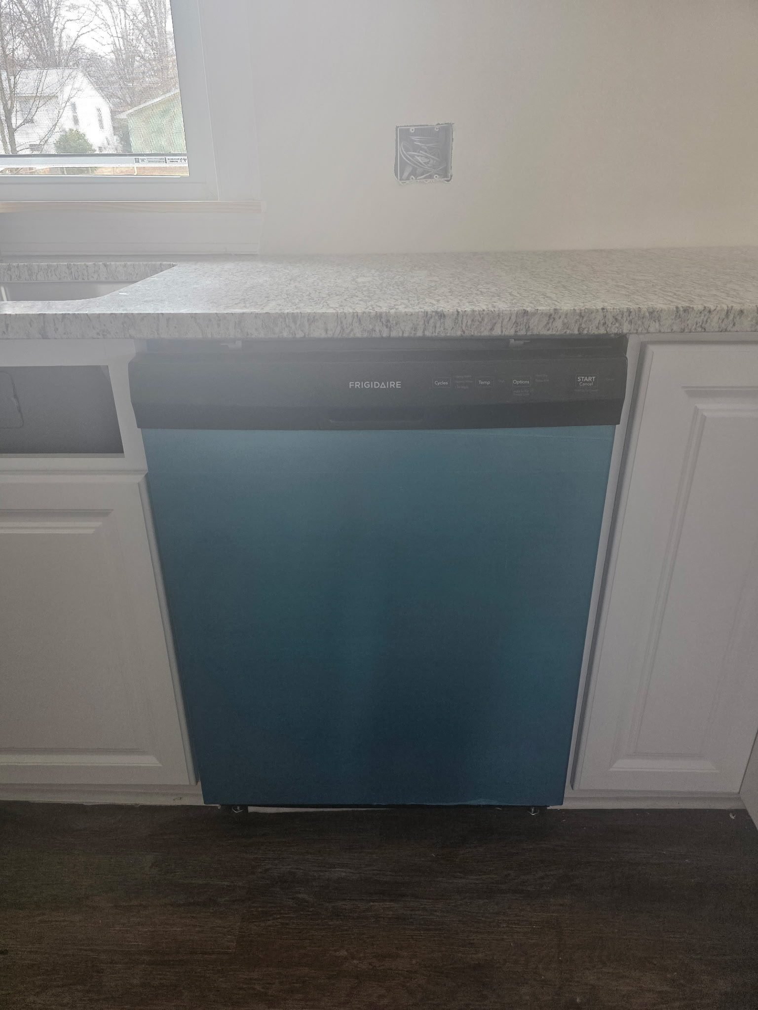 Blue dishwasher installed under a granite countertop next to white kitchen cabinets.