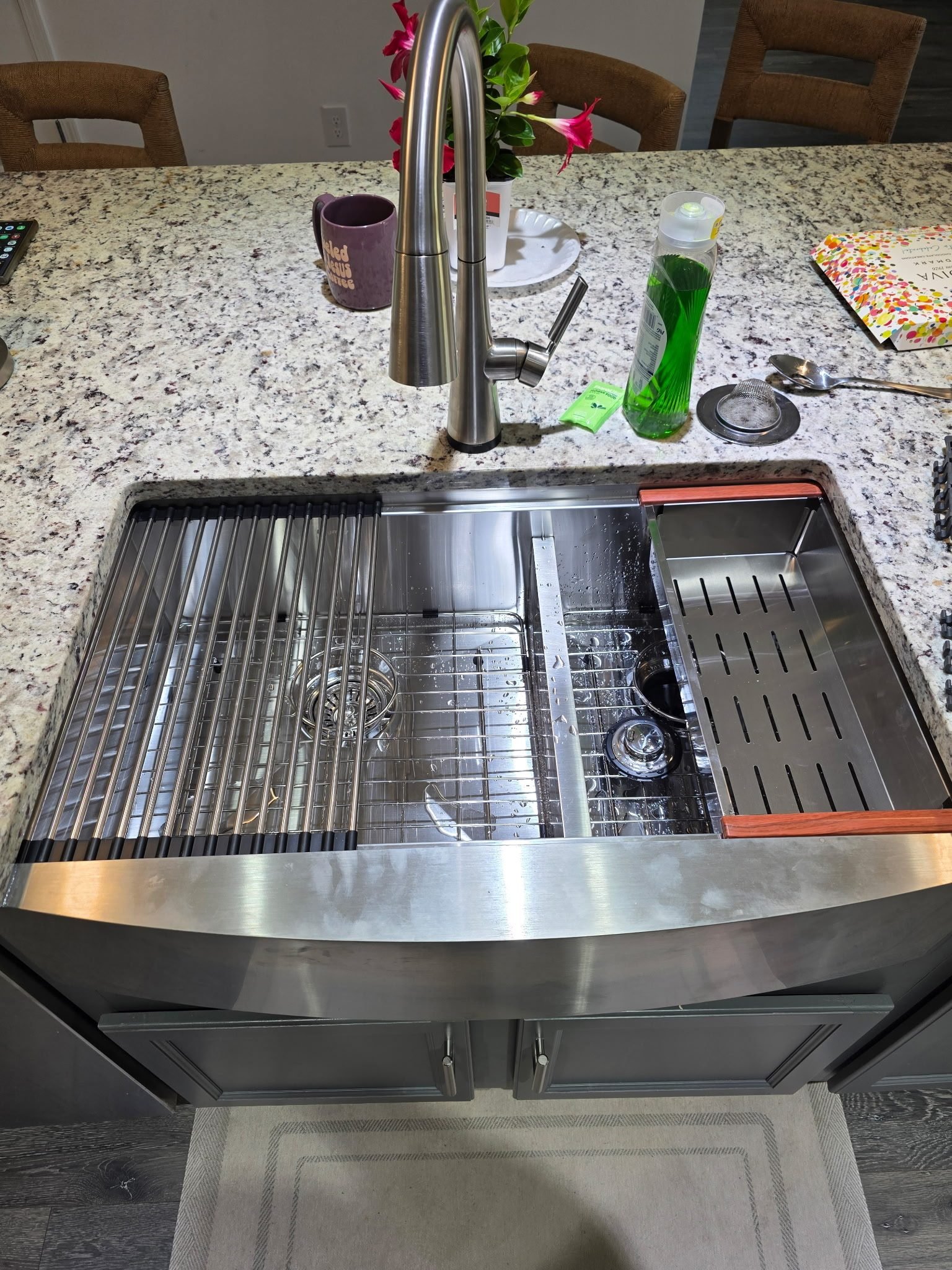 Stainless steel farmhouse-style kitchen sink with a pull-down faucet on a granite island countertop.