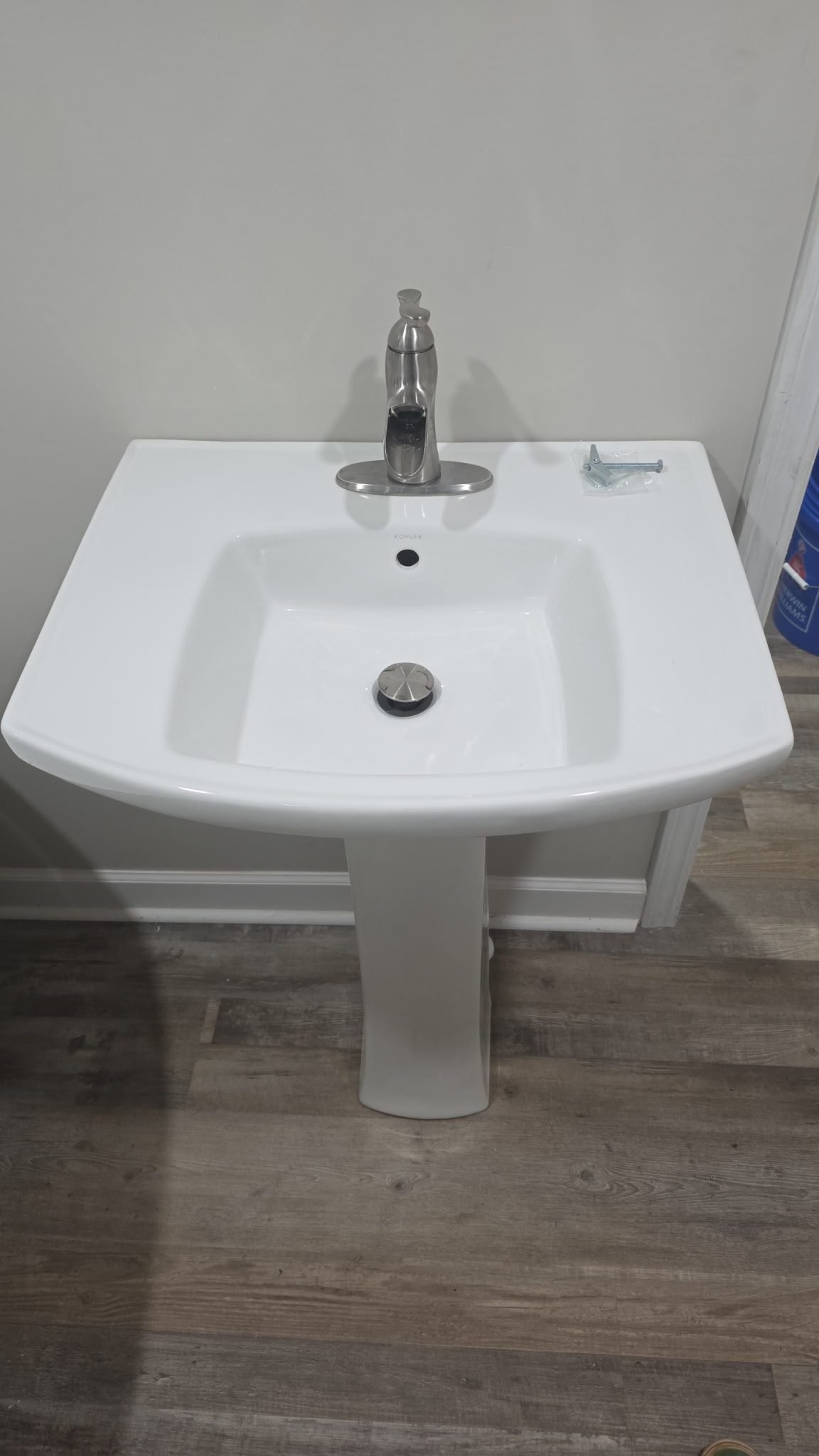 White pedestal bathroom sink with a brushed nickel faucet and pop-up drain, newly installed.