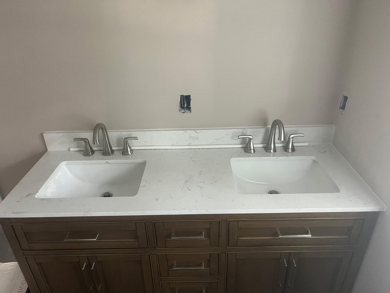 White quartz double undermount sink vanity top with brushed nickel faucets on a dark wood cabinet.