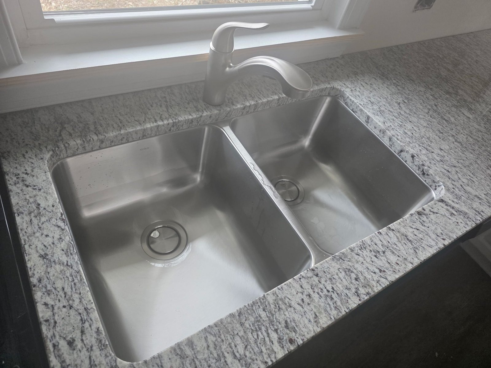 Stainless steel double-bowl kitchen sink with a brushed nickel pull-out faucet, newly installed under a window.
