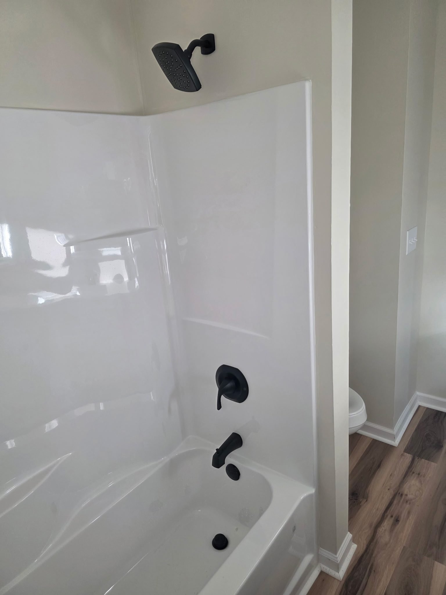 White fiberglass tub-shower combo with matte black shower head, valve, and tub spout near a toilet.