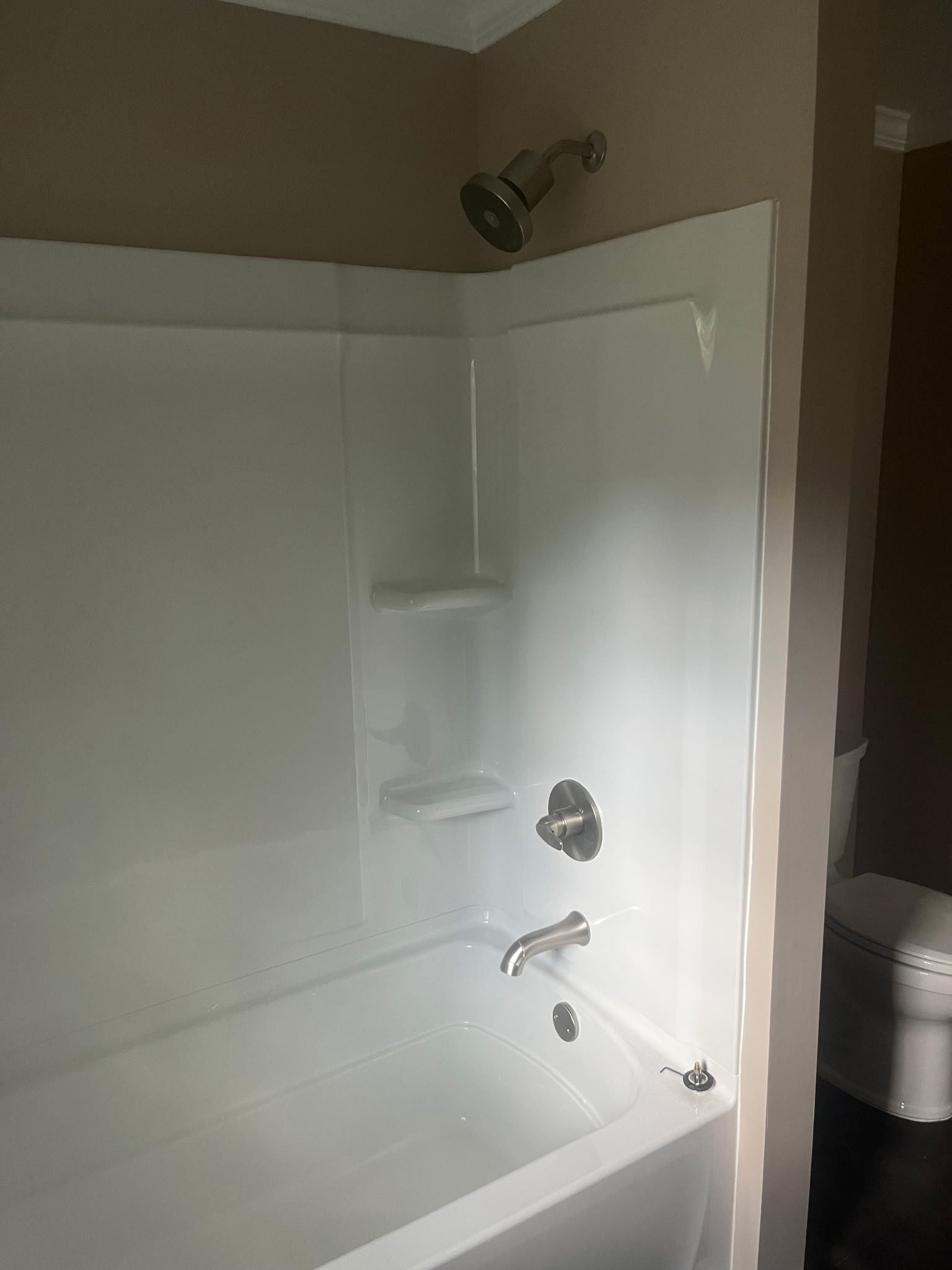 White fiberglass tub-shower combo with brushed nickel shower head, valve, and tub spout next to a toilet.