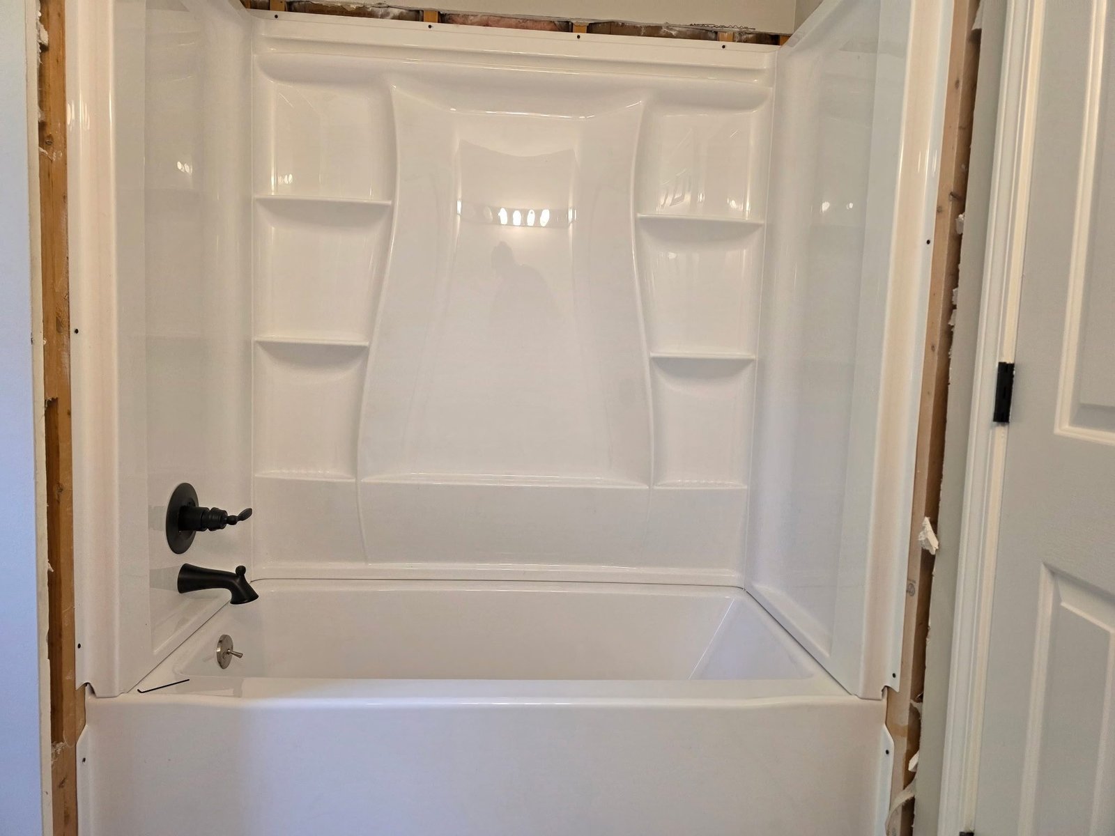 White fiberglass tub-shower surround installed in a framed bathroom with an oil-rubbed bronze faucet and valve.