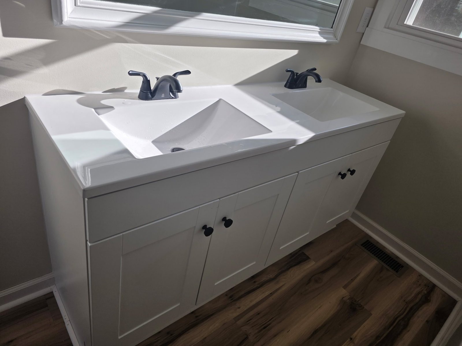 White double-sink bathroom vanity with matte black faucets newly installed under a window.
