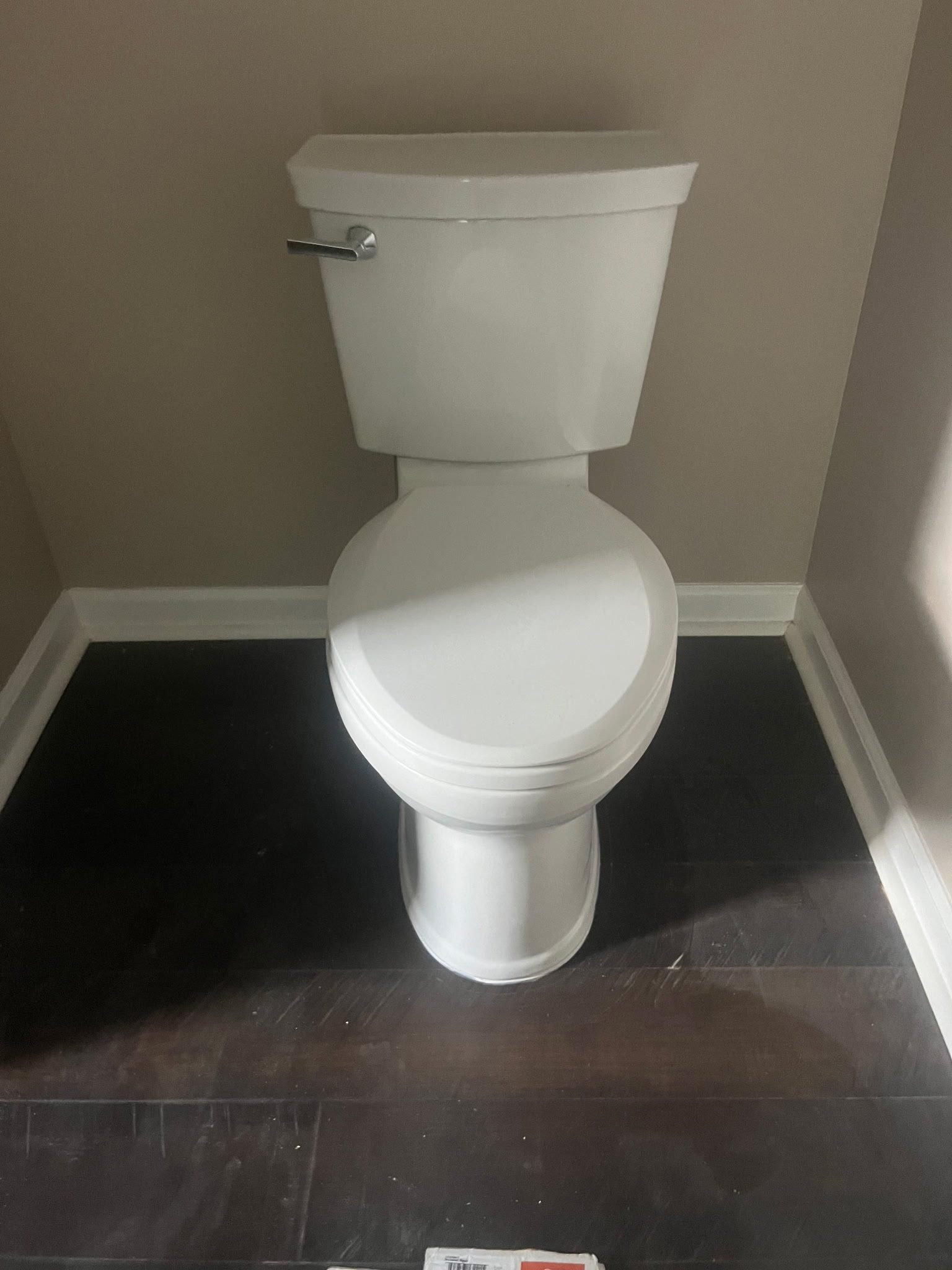 White two-piece toilet newly installed on wood-look flooring in a corner bathroom.