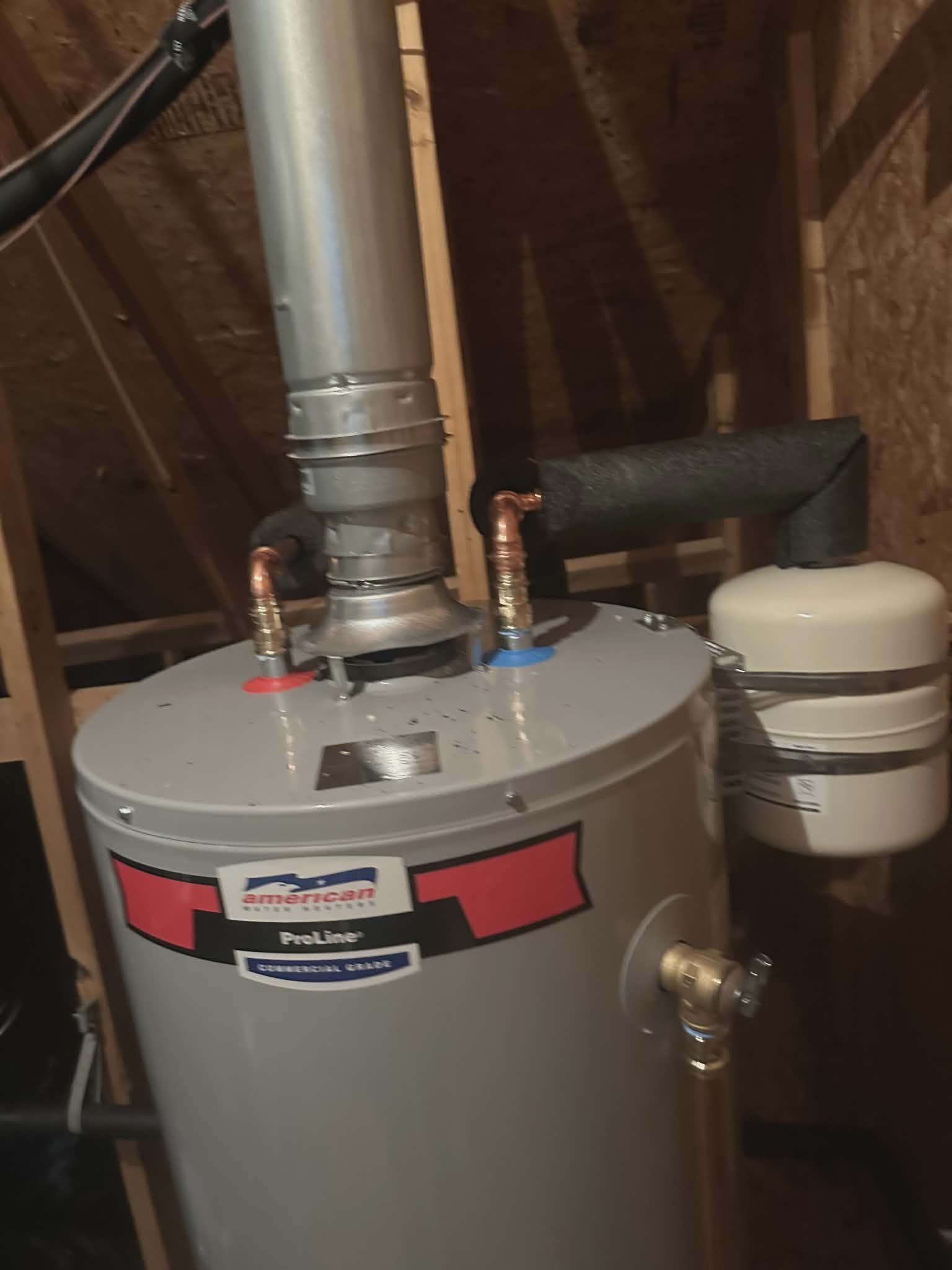 Commercial-grade gas water heater installed in an attic with a metal flue vent.