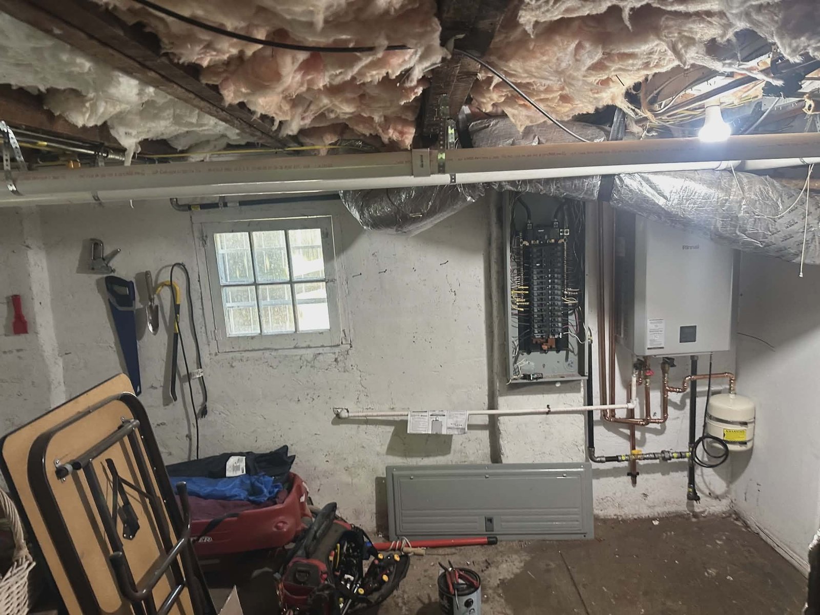 Unfinished basement utility area with a gas water heater, copper piping, and an expansion tank.