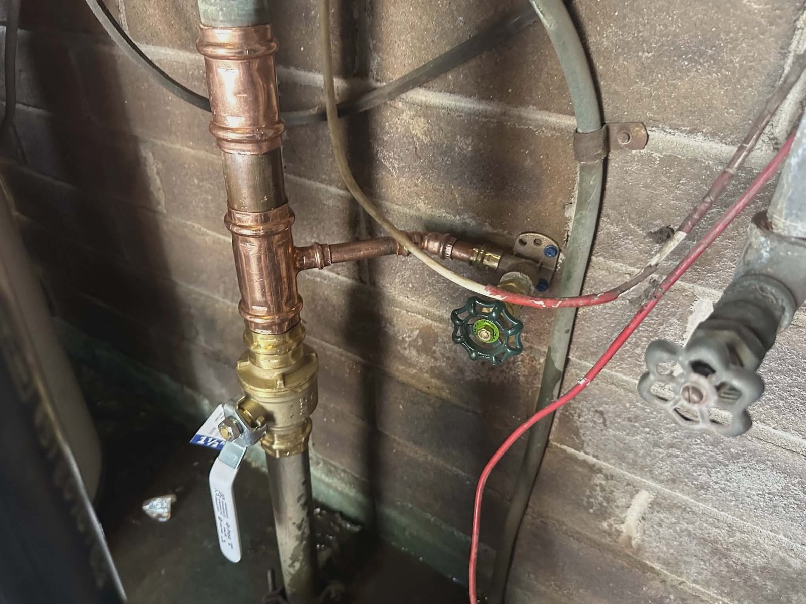 Close-up of copper pipe with a brass ball valve and shutoff near a brick wall.