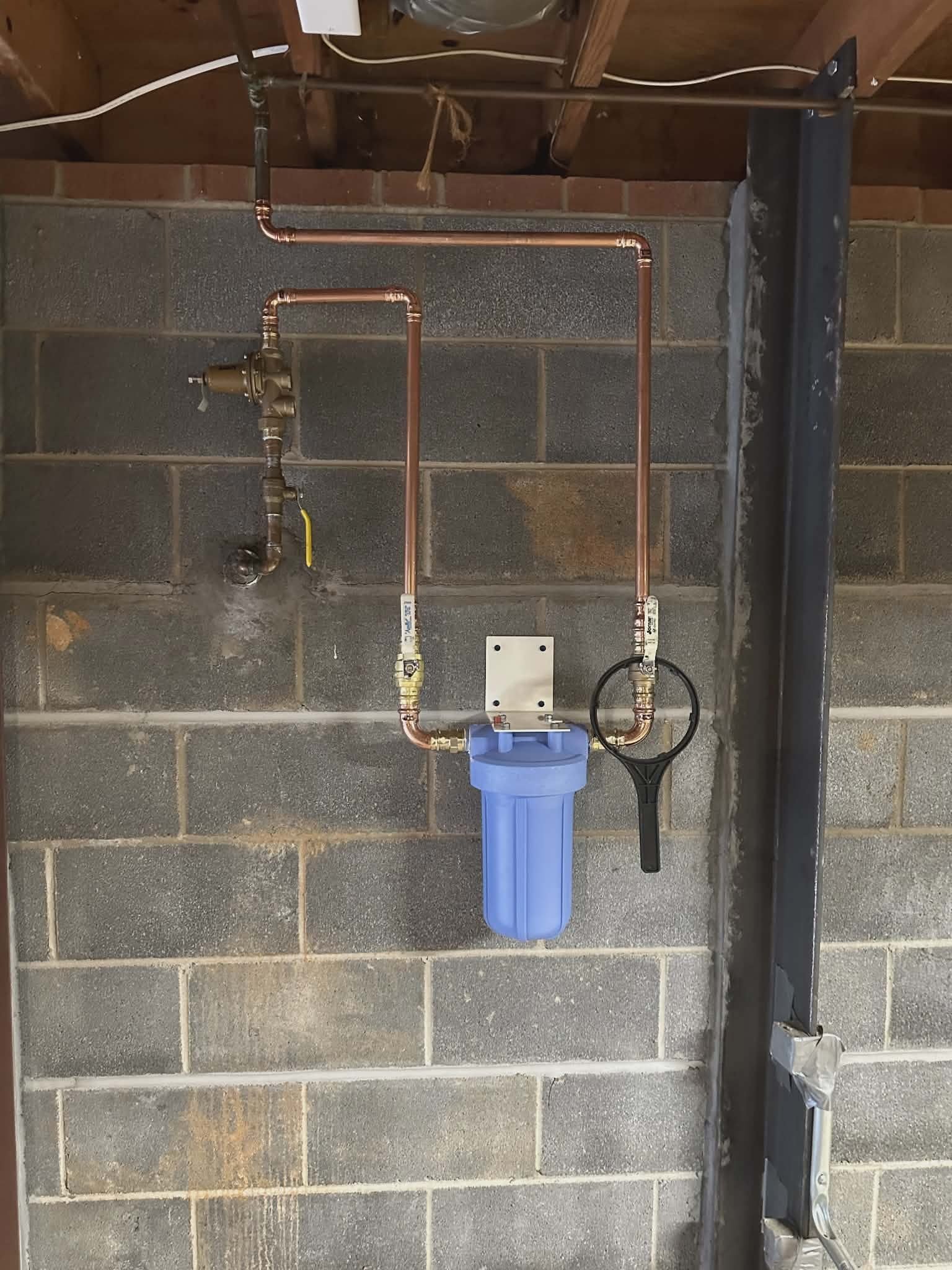 Copper piping with a shutoff valve and sediment filter housing mounted on a basement wall.