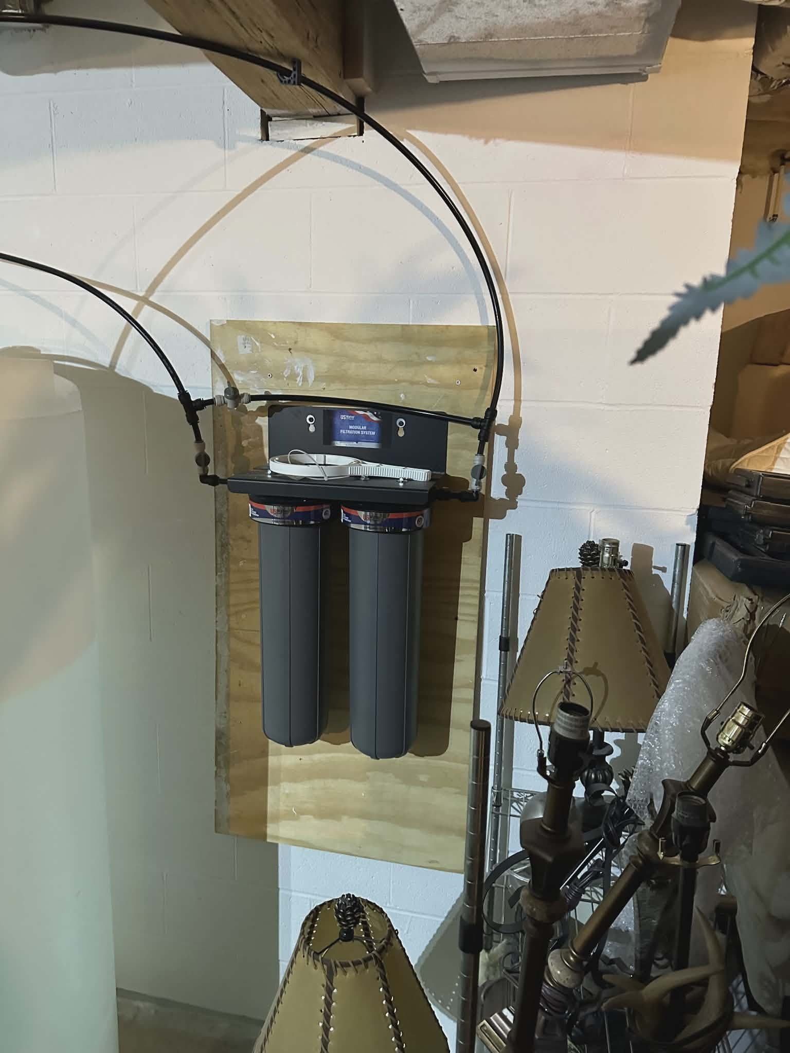 Two gray water filter housings mounted on a board hanging from ceiling joists.