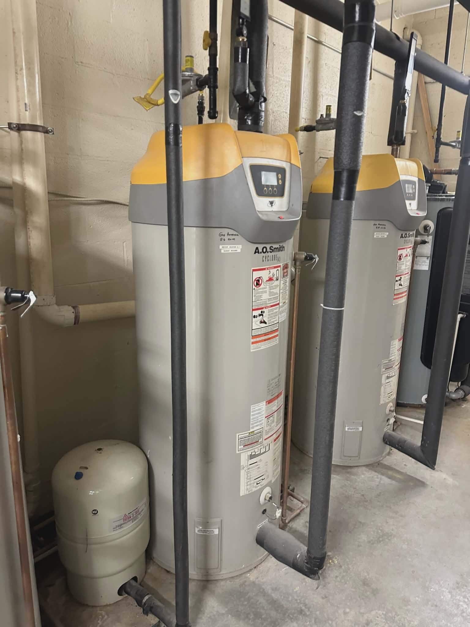 Two commercial-grade gas water heaters installed side by side with a small expansion tank.