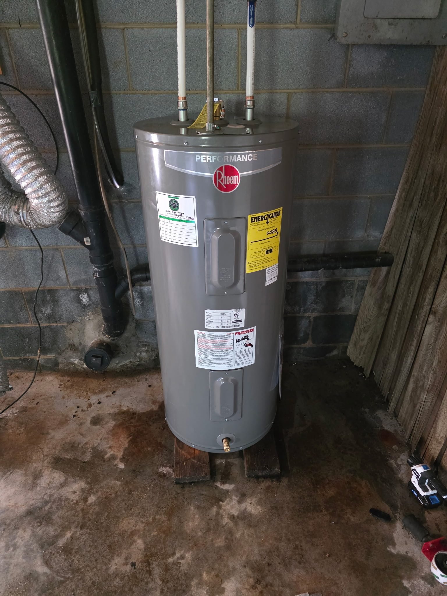 Electric water heater installed in a basement on wood blocking with copper supply lines.