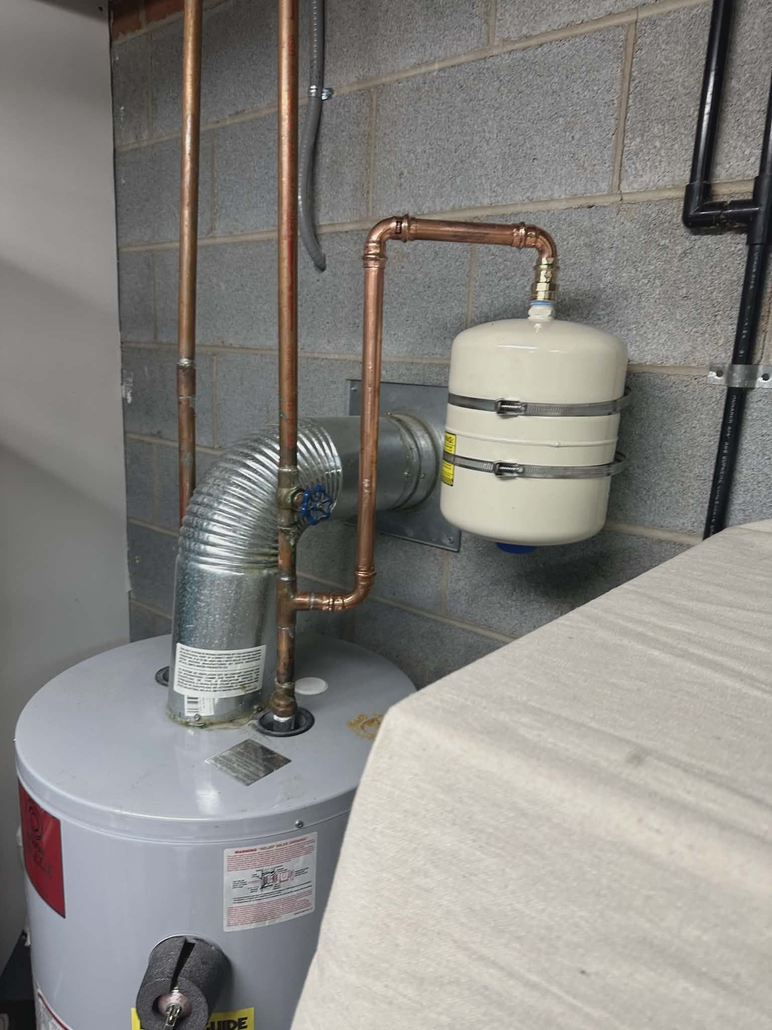 Small expansion tank mounted with copper piping above a gas water heater.