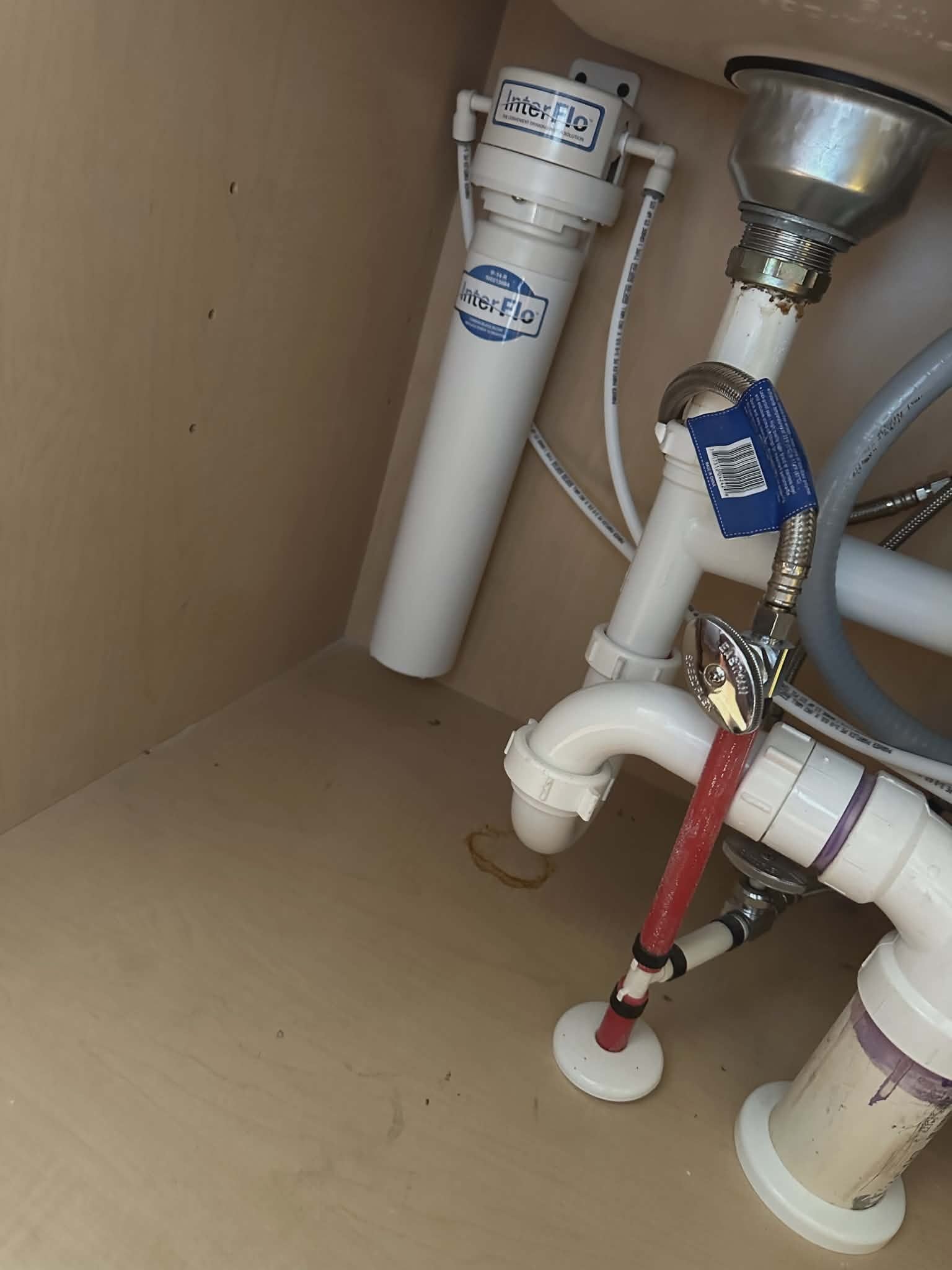 Water filtration cartridges and PVC drain piping installed under a kitchen sink.