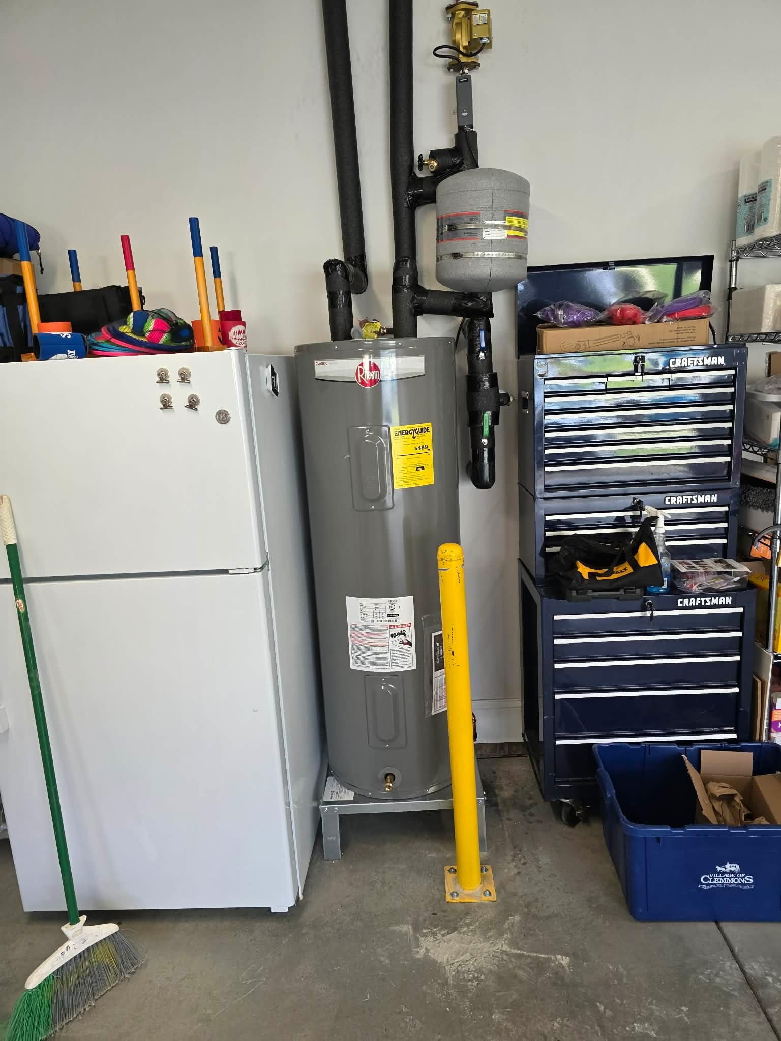 Gas water heater installed in a garage with black vent piping and an expansion tank above.