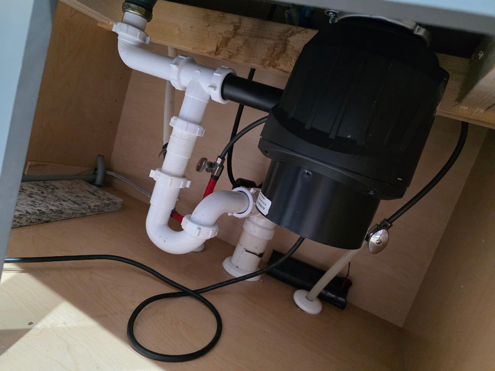 Garbage disposal and PVC drain piping installed under a kitchen sink with a shutoff valve.