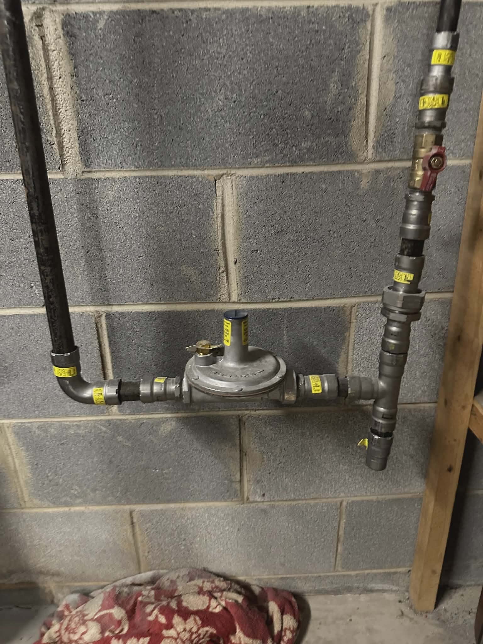Galvanized gas line with a pressure regulator and tagged shutoff valves mounted on a wall.