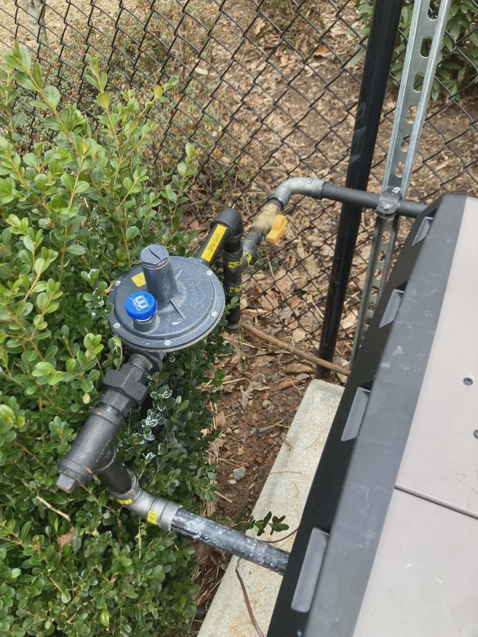 Gas pressure regulator and shutoff valves mounted on a low wall near an outdoor HVAC unit.