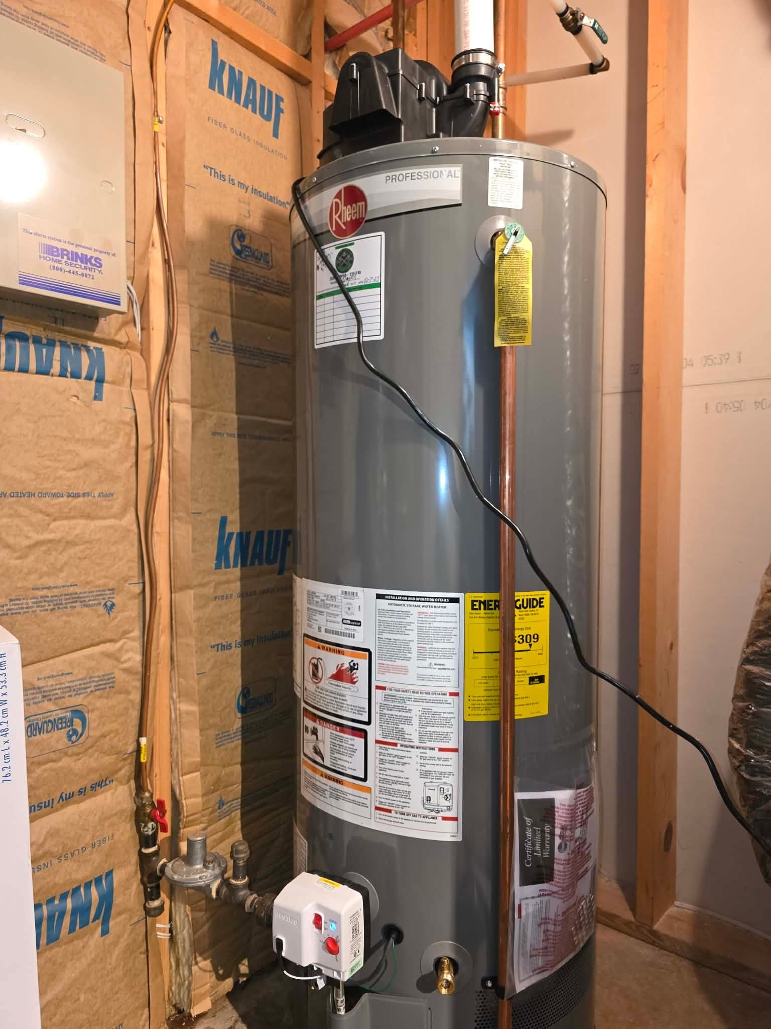 Gas water heater installed against an insulated wall with a gas control valve visible.