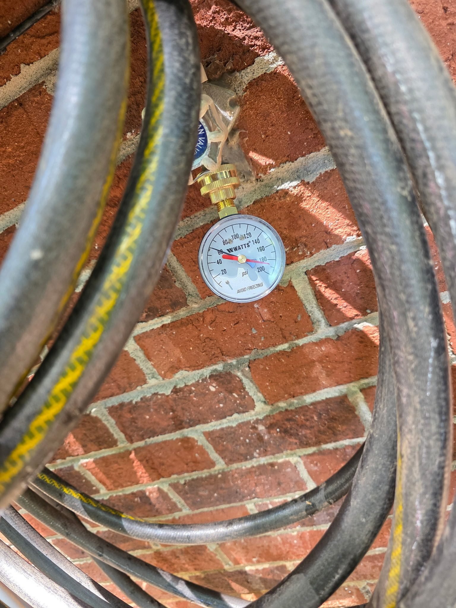 Close-up of a pressure gauge attached to an outdoor hose bib against a brick wall.