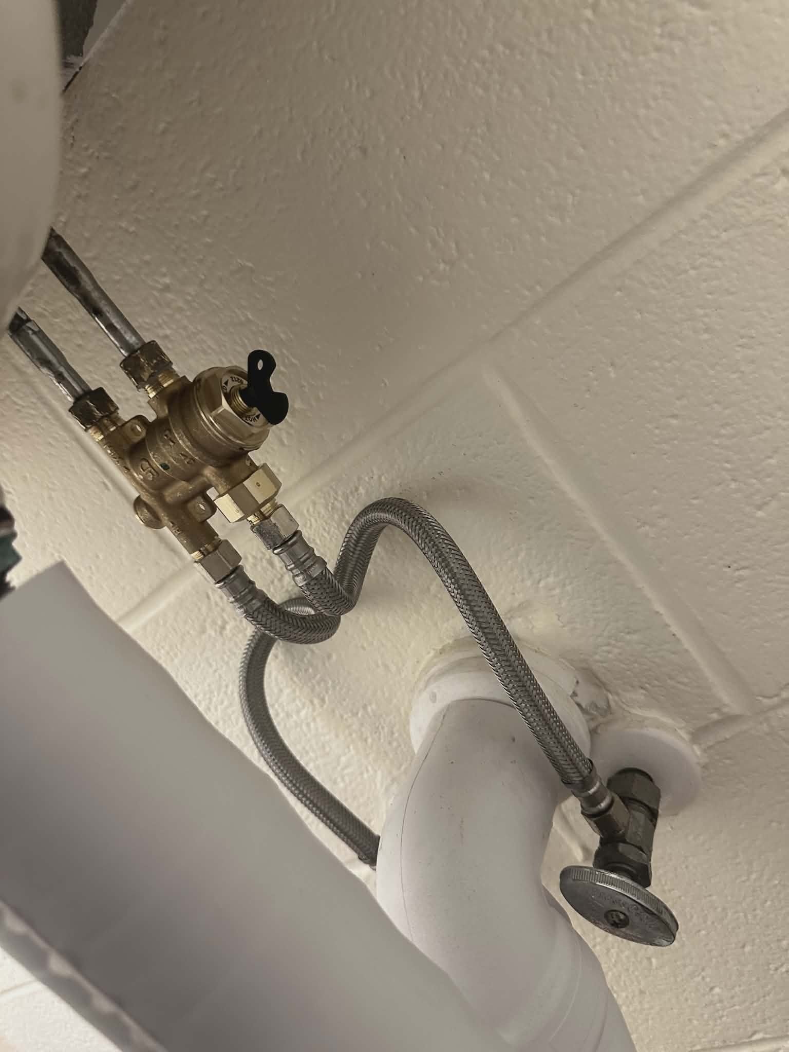 Close-up of a brass pressure-reducing valve assembly with braided supply lines.