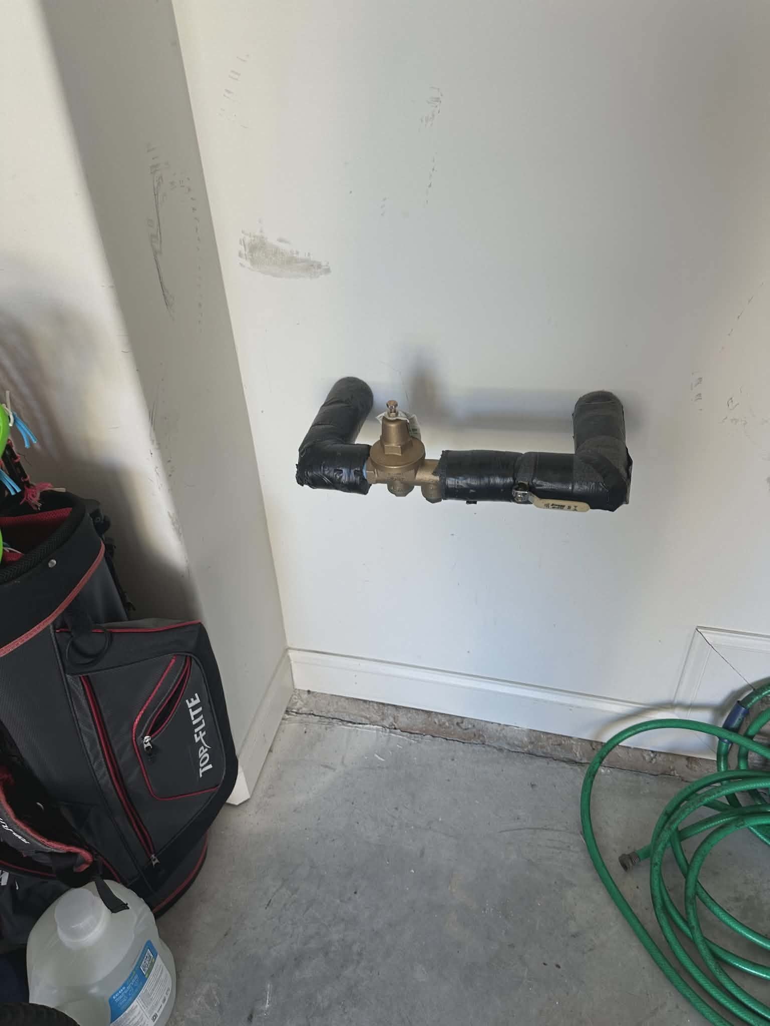 Brass pressure-reducing valve installed between two insulated pipes mounted on a garage wall.
