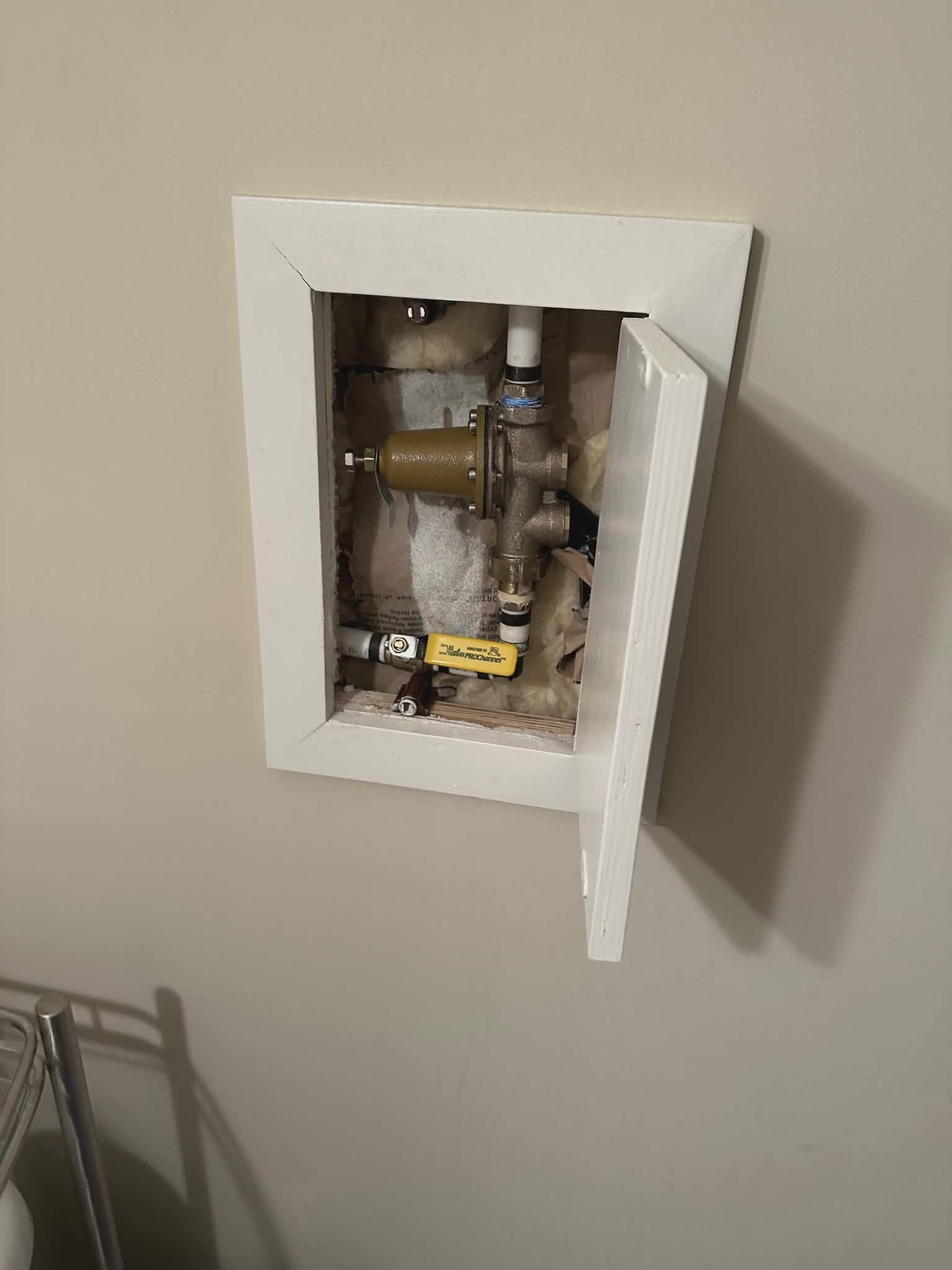Recessed wall access panel revealing a brass pressure-reducing valve and copper piping inside.