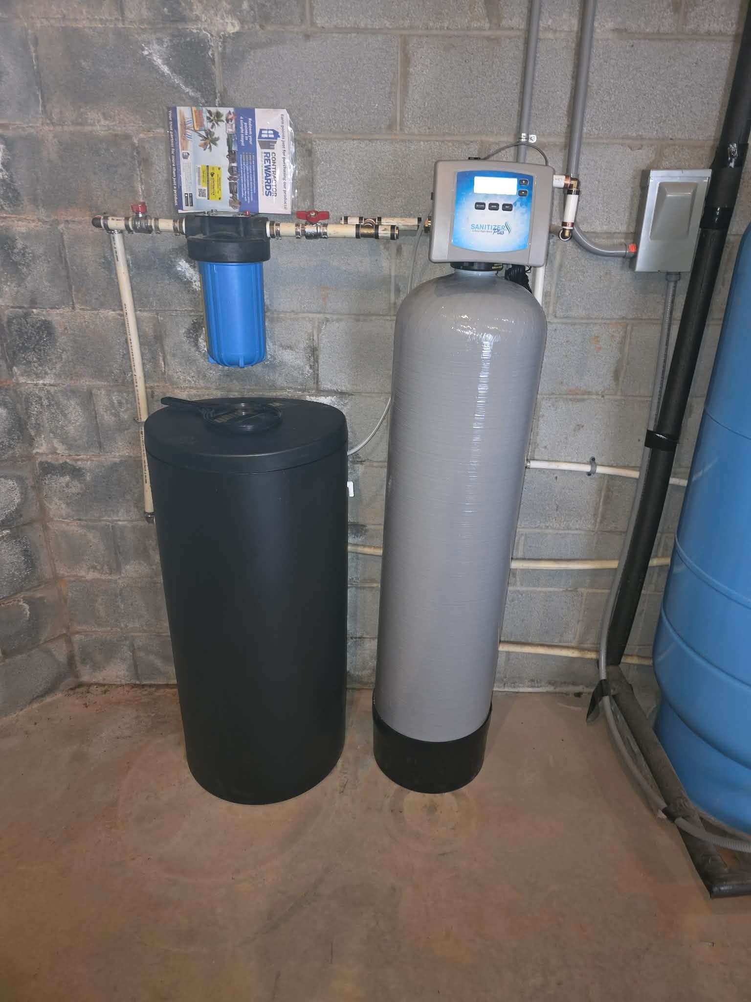 Sediment filter canister mounted between PVC pipes above a water softener tank.