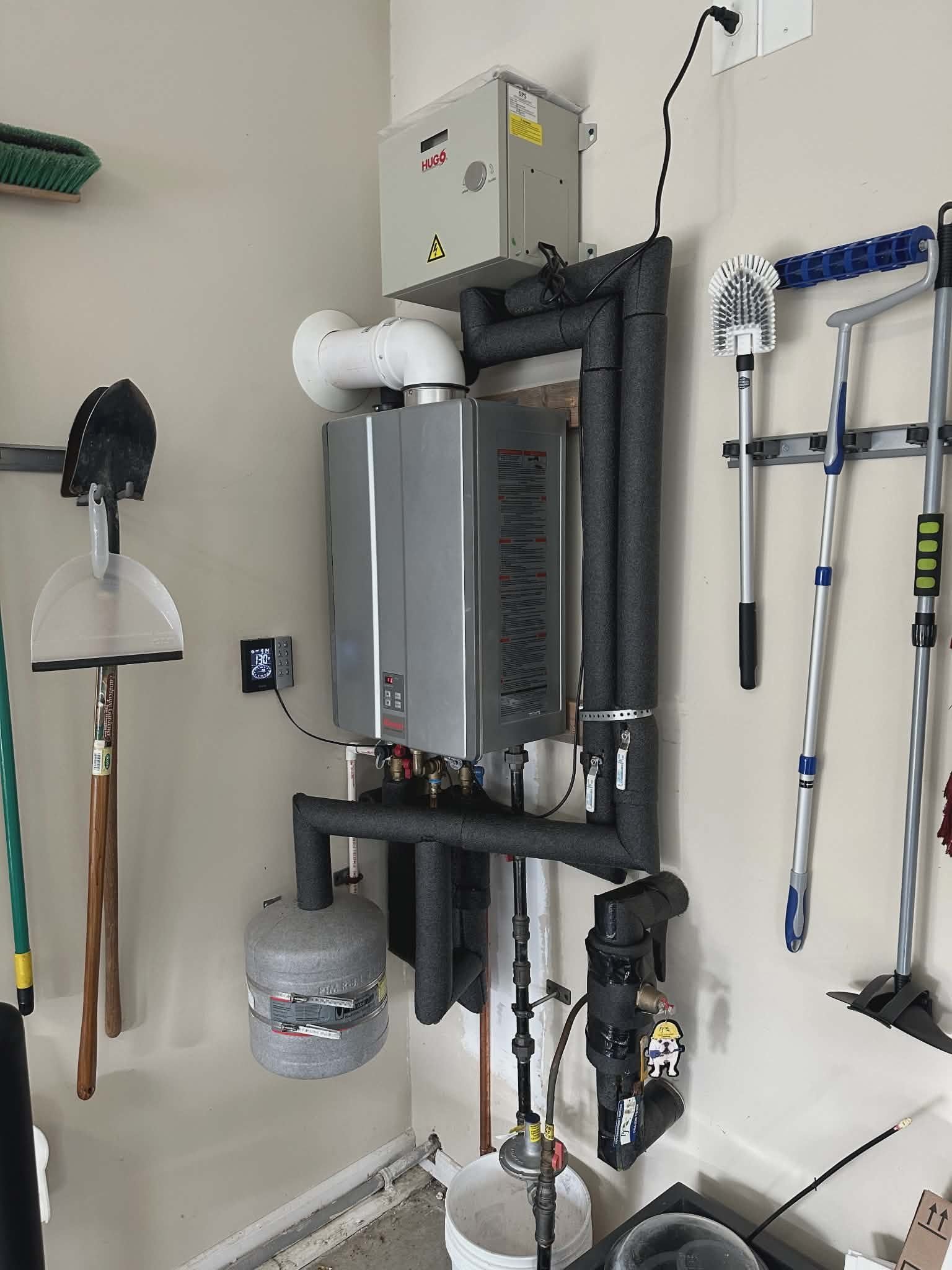 Tankless water heater mounted in a garage above a small expansion tank.