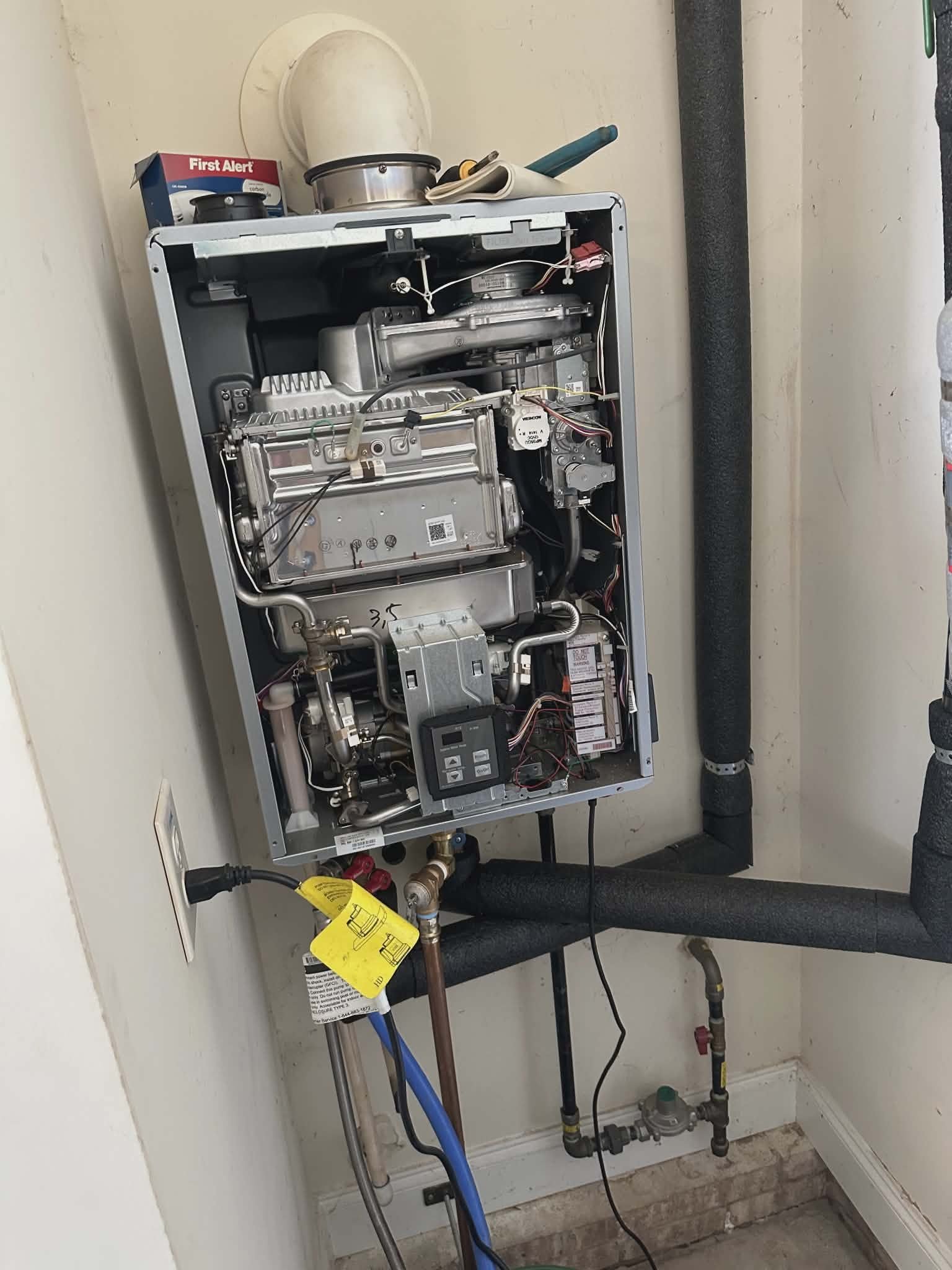 Open tankless water heater unit with the front cover removed, exposing the internal heat exchanger.
