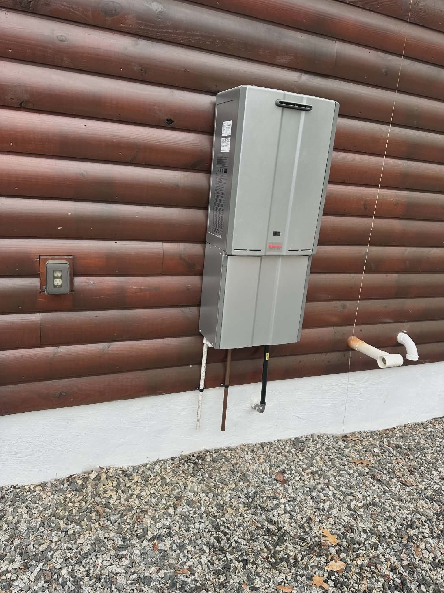 Tankless water heater mounted on exterior siding with a copper drain line.