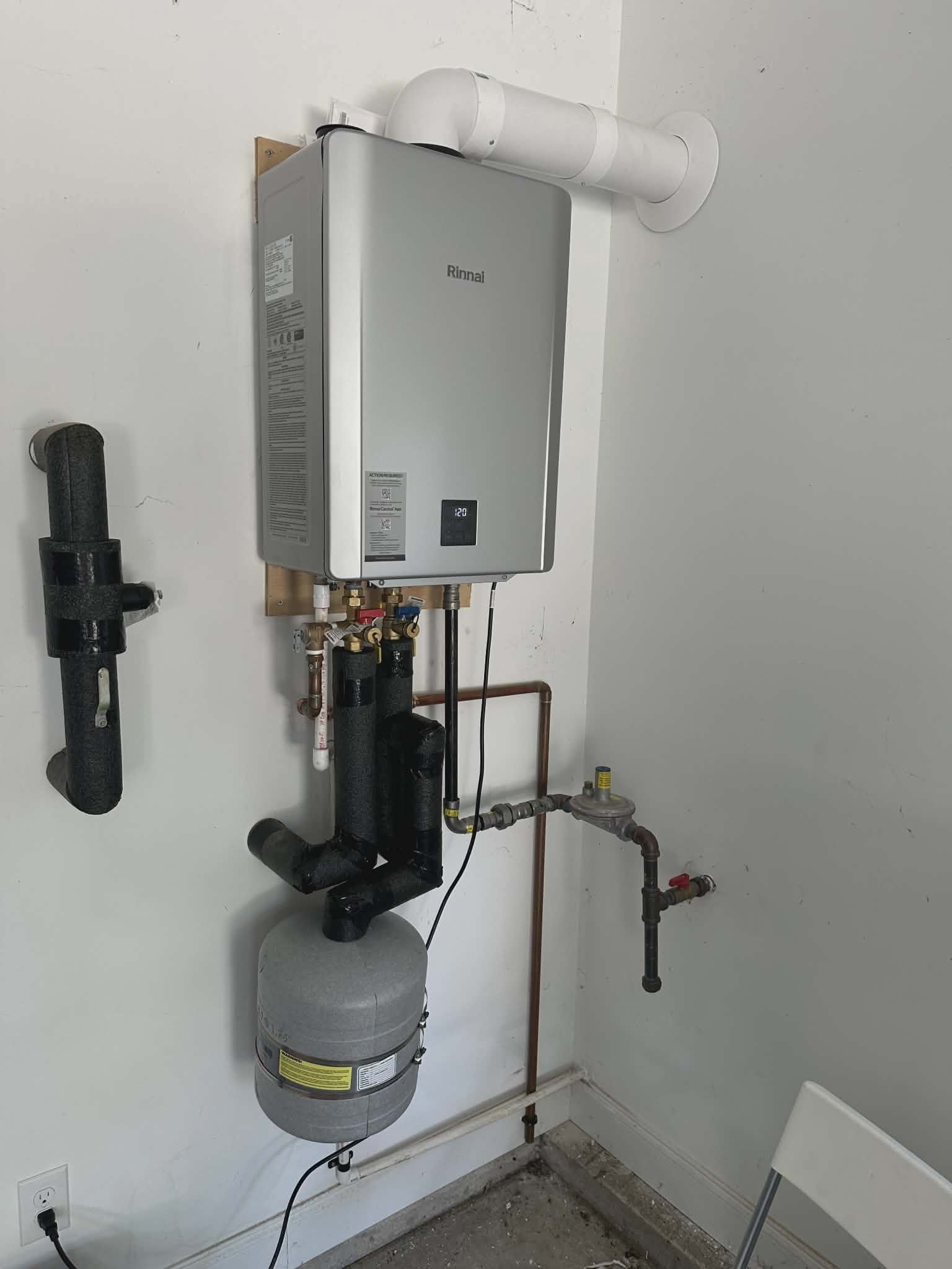 Tankless water heater mounted on an interior wall above a small expansion tank with copper supply lines.