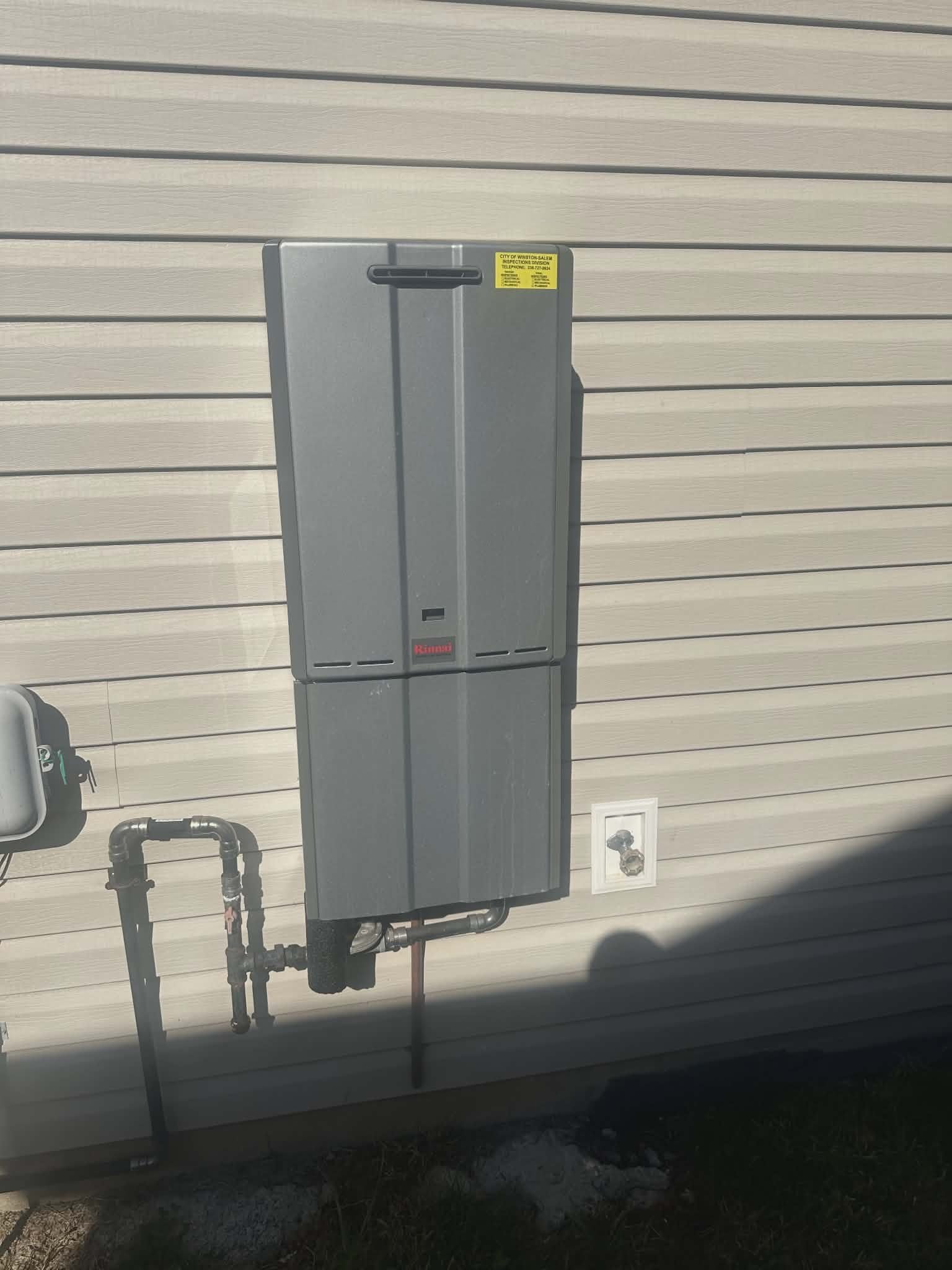 Tankless water heater mounted on exterior vinyl siding with copper drain piping.