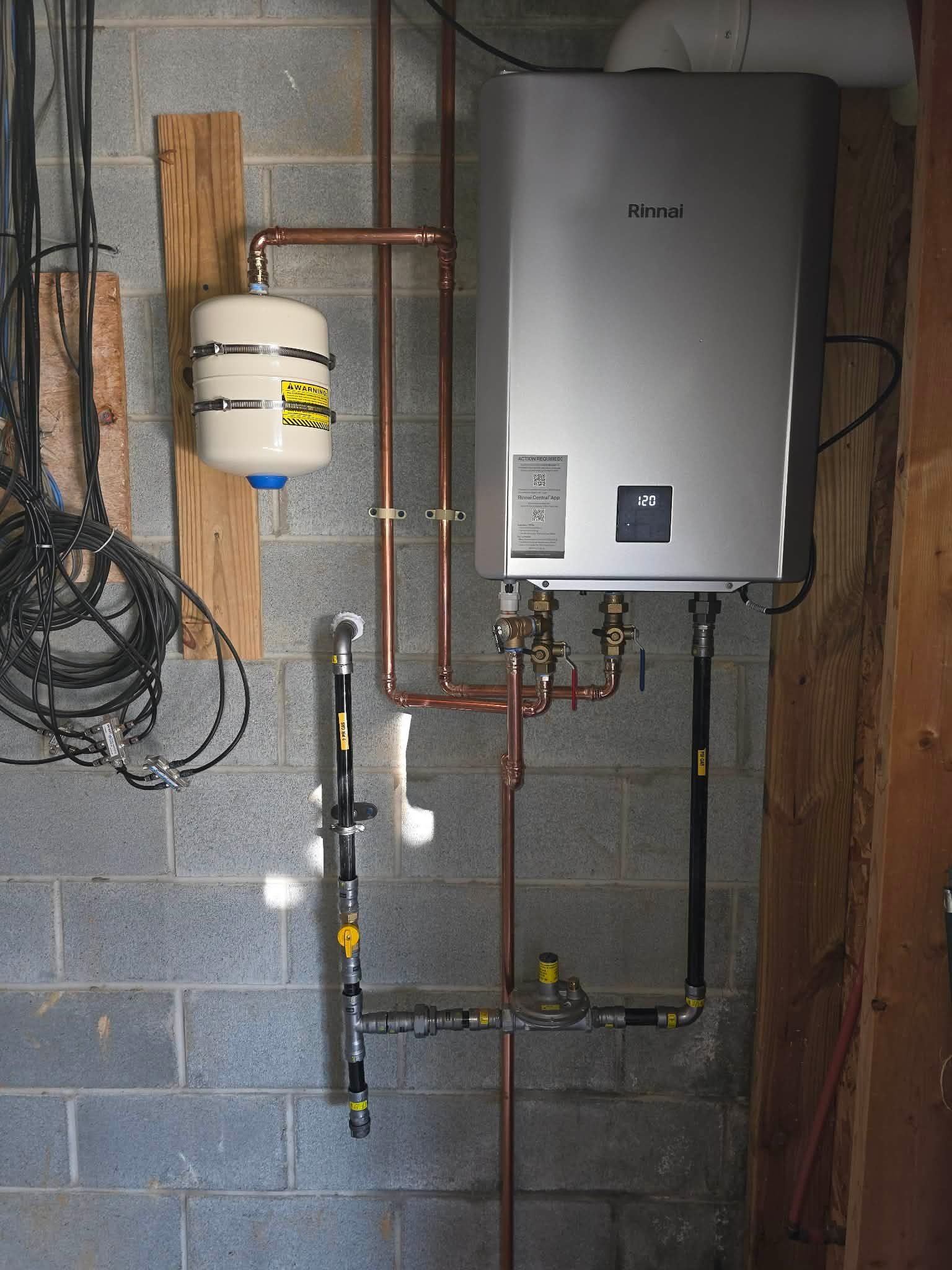 Tankless water heater mounted on a wall with copper piping and a small expansion tank.
