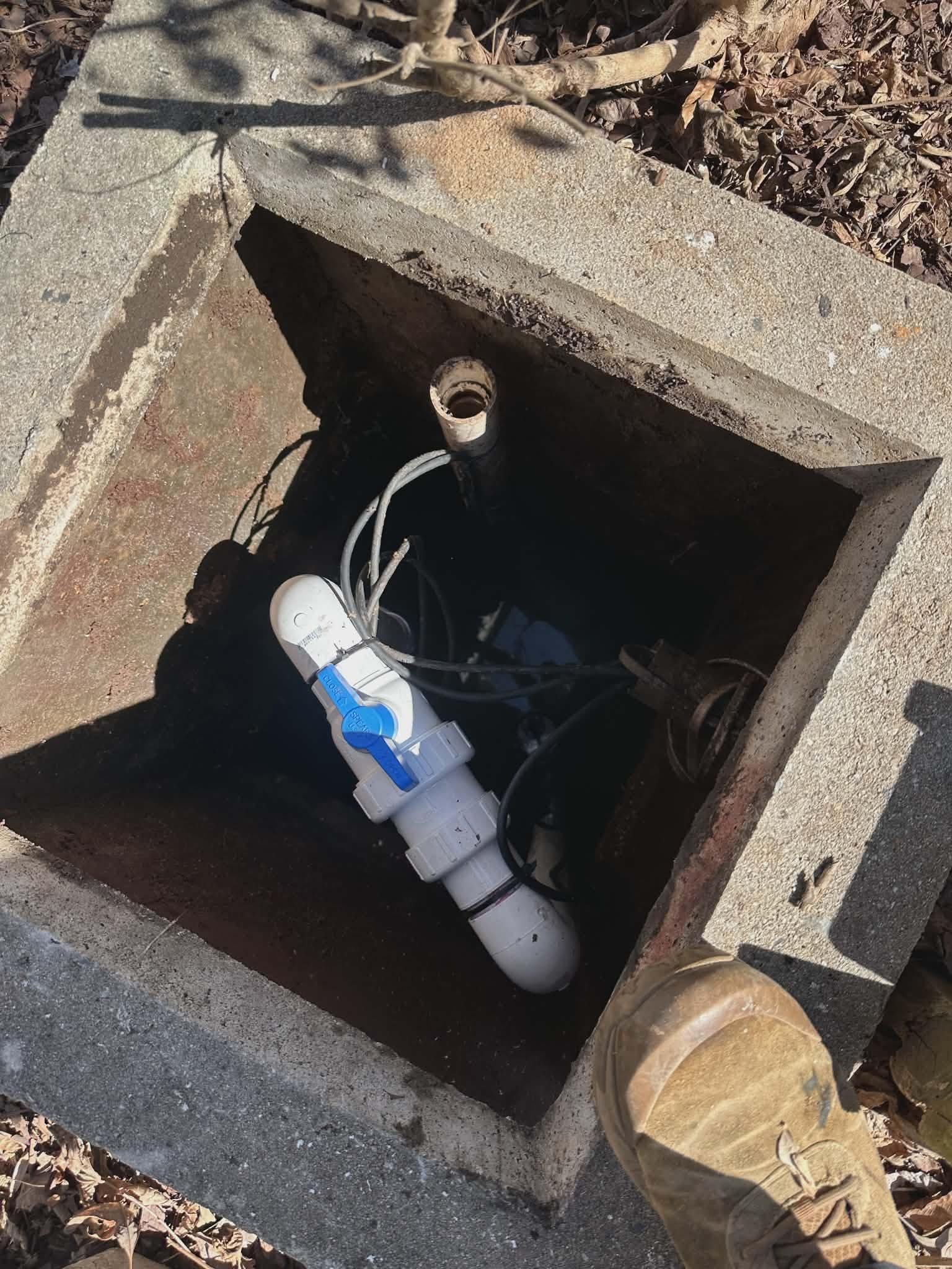 Overhead view into an underground utility valve box showing a PVC shutoff valve assembly.