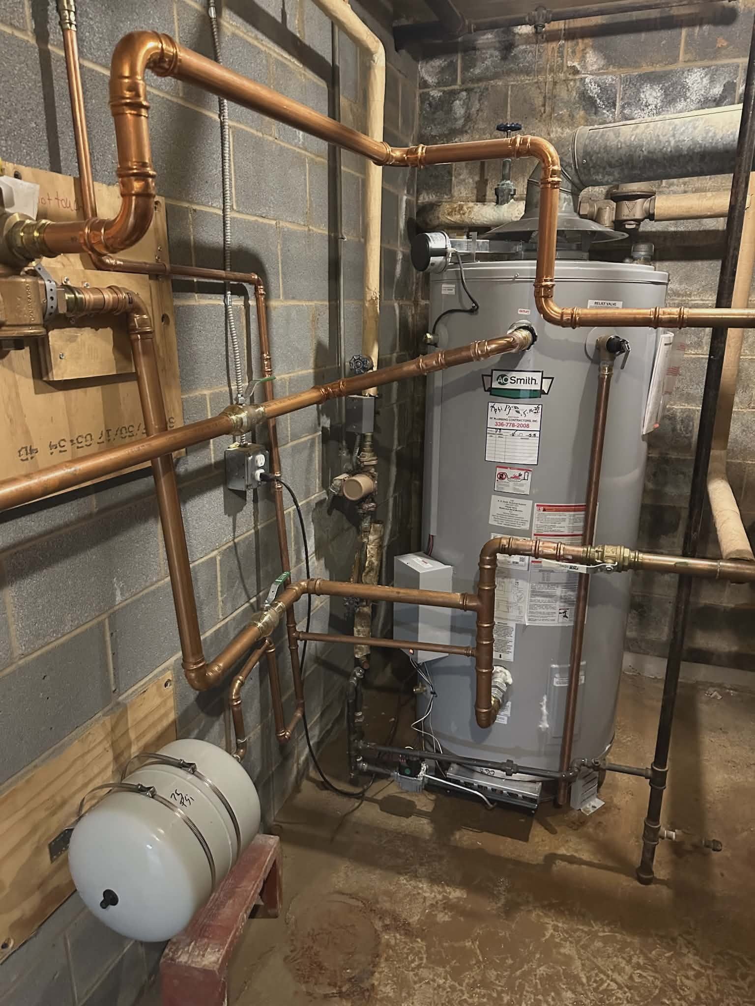 Gas water heater with an extensive copper piping network installed in a basement utility room.