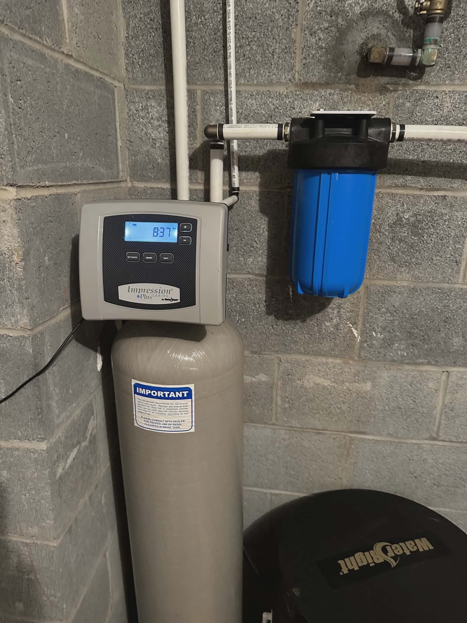 Water softener resin tank with a digital control head and sediment filter mounted on a wall.