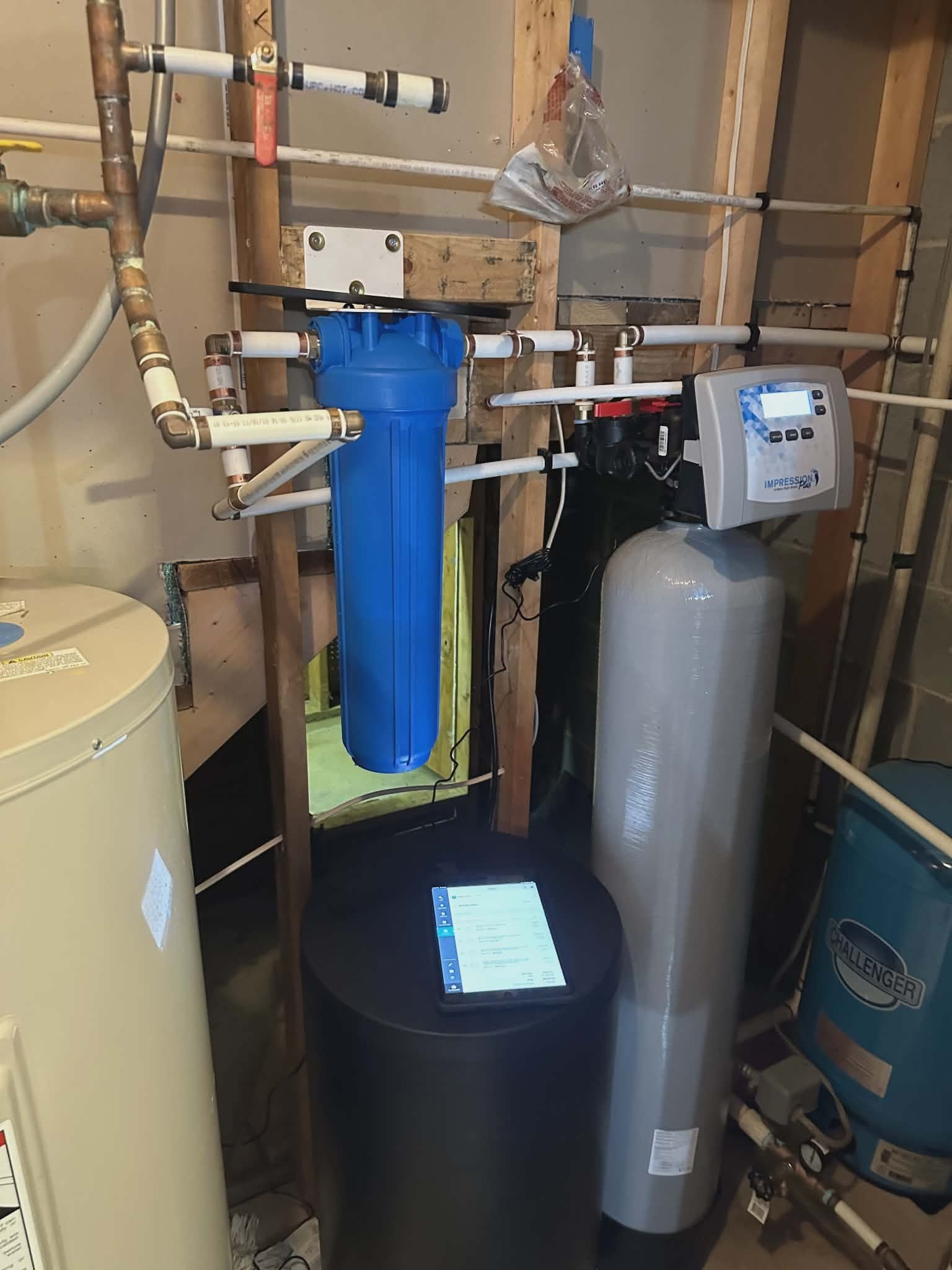 Water softener system with a sediment filter, resin tank, control head, and pressure tank in a basement.