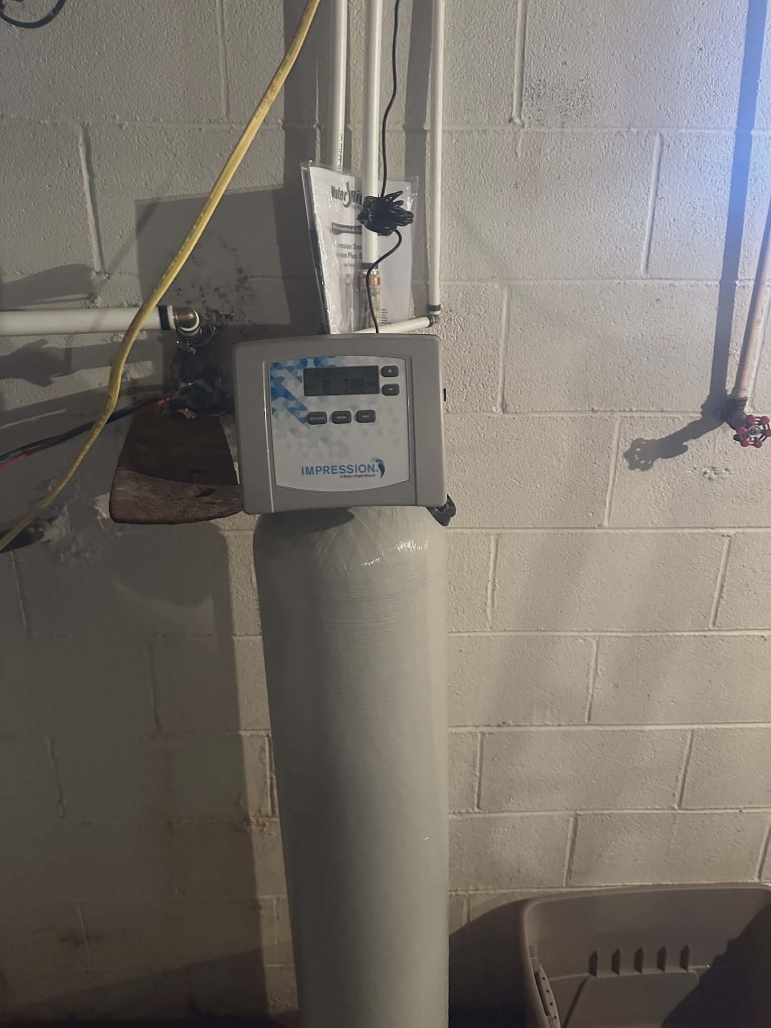 Water softener resin tank with a digital control head mounted on a wall.