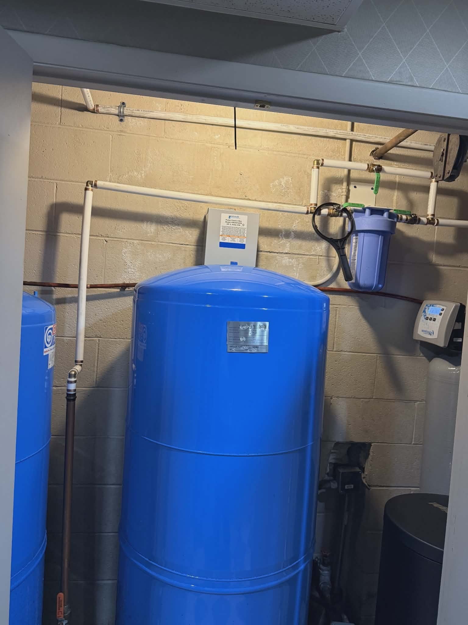 Well pressure tank with a control head and inline filter mounted in a utility closet.