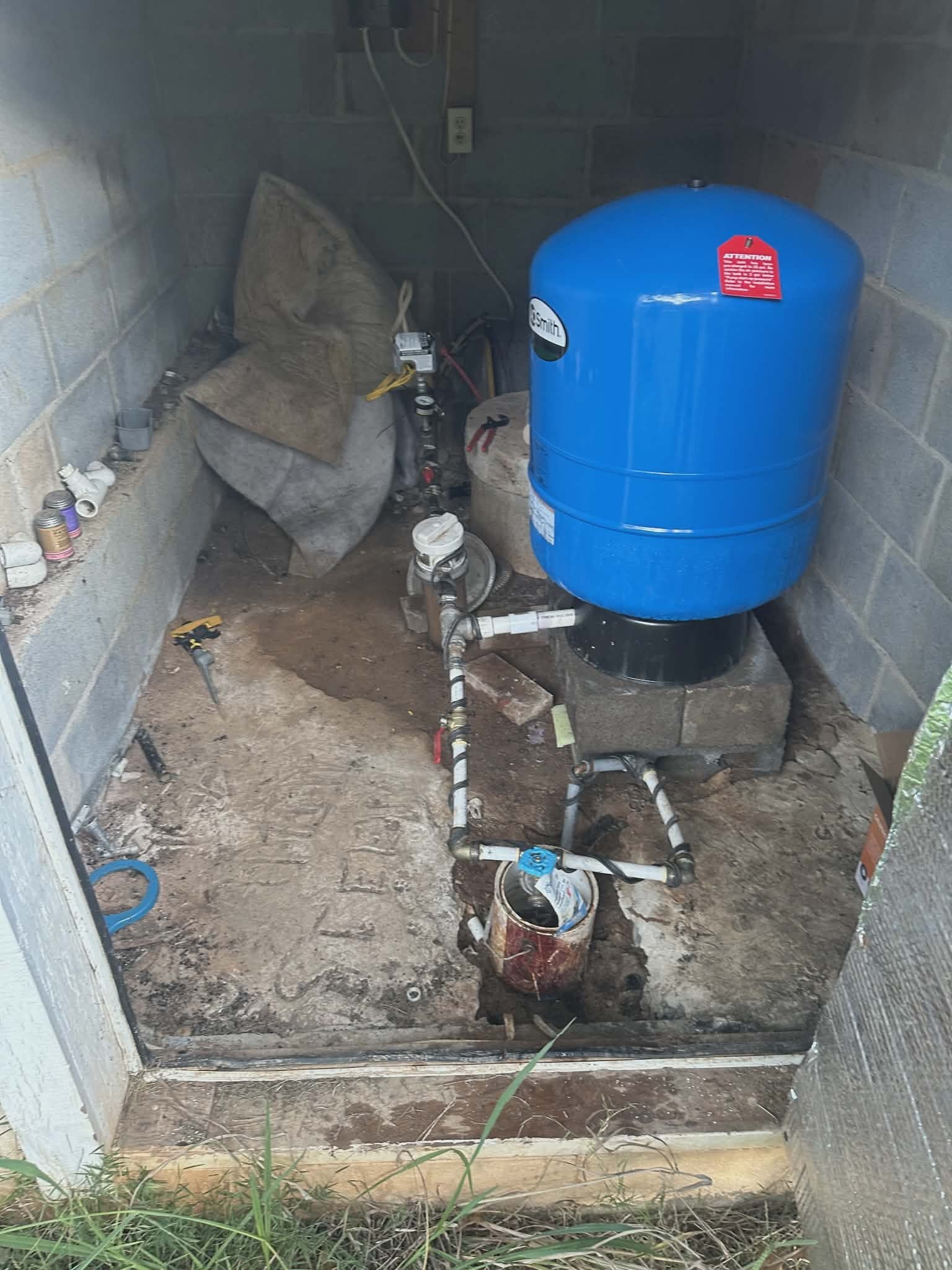 Well pressure tank installed in an outdoor well house with exposed PVC piping and wiring.