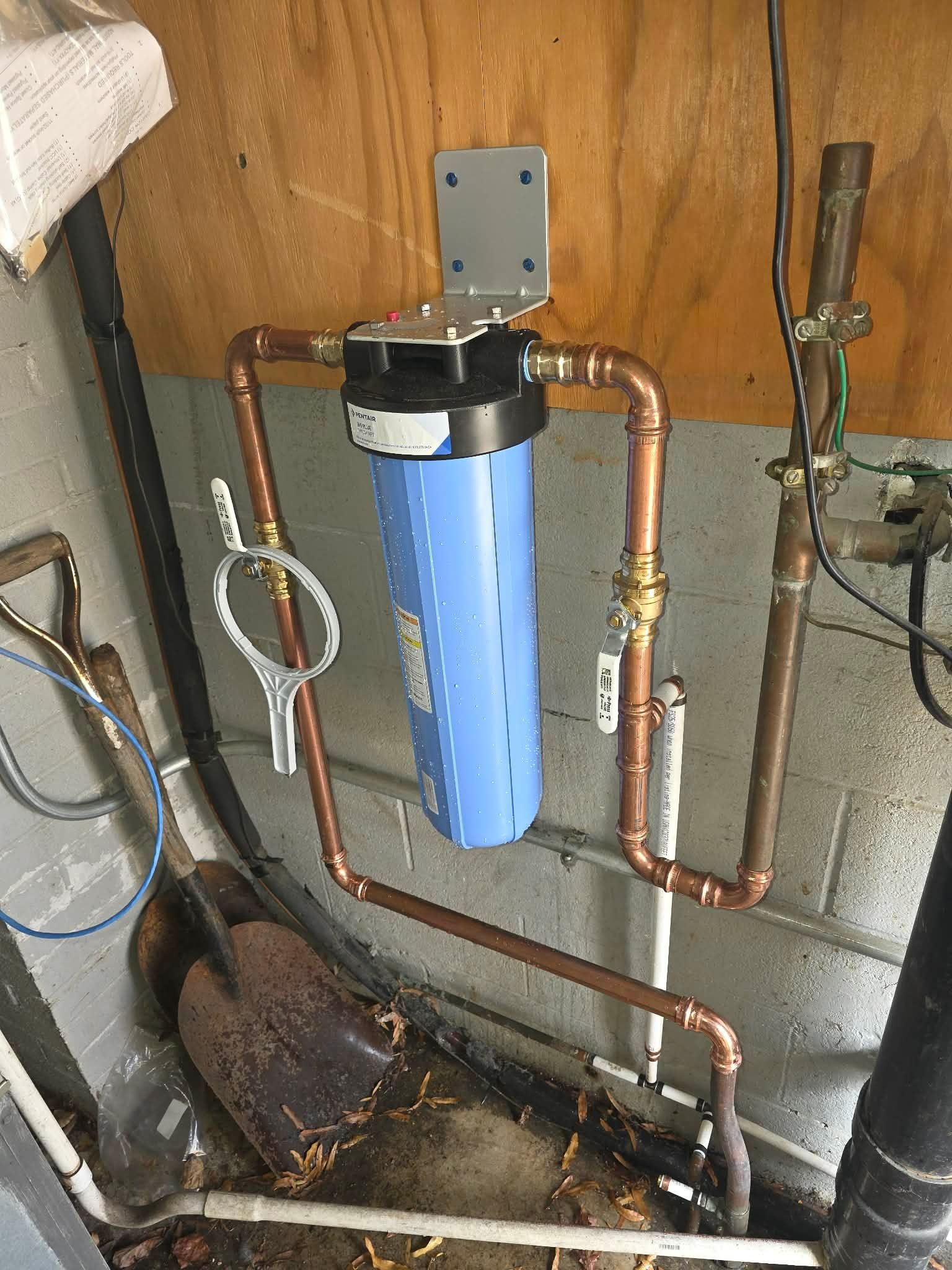 Whole-house water filter mounted on copper piping against a basement wall.