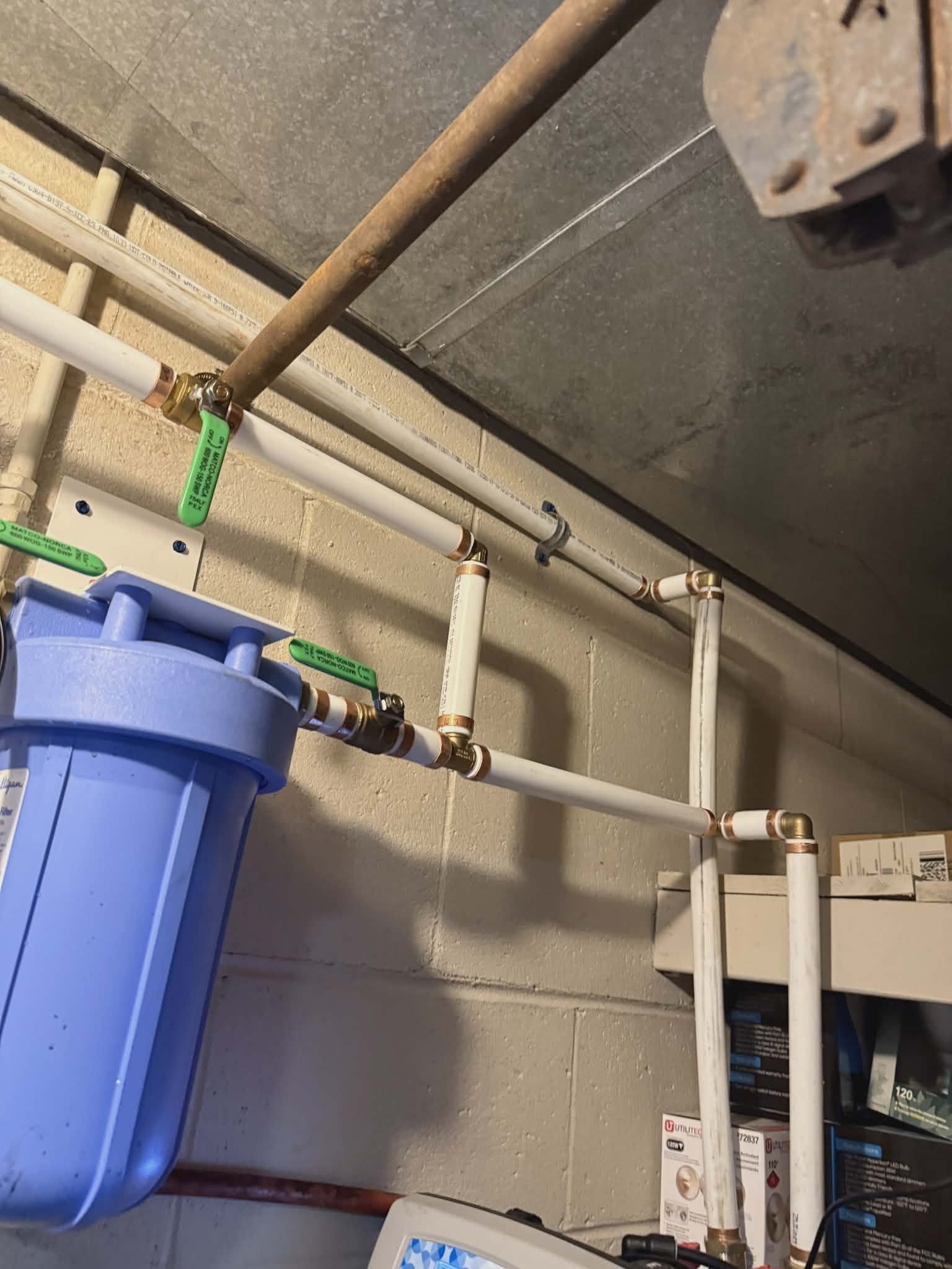 Whole-house filter mounted on a wall with PVC piping and tagged shutoff valves.